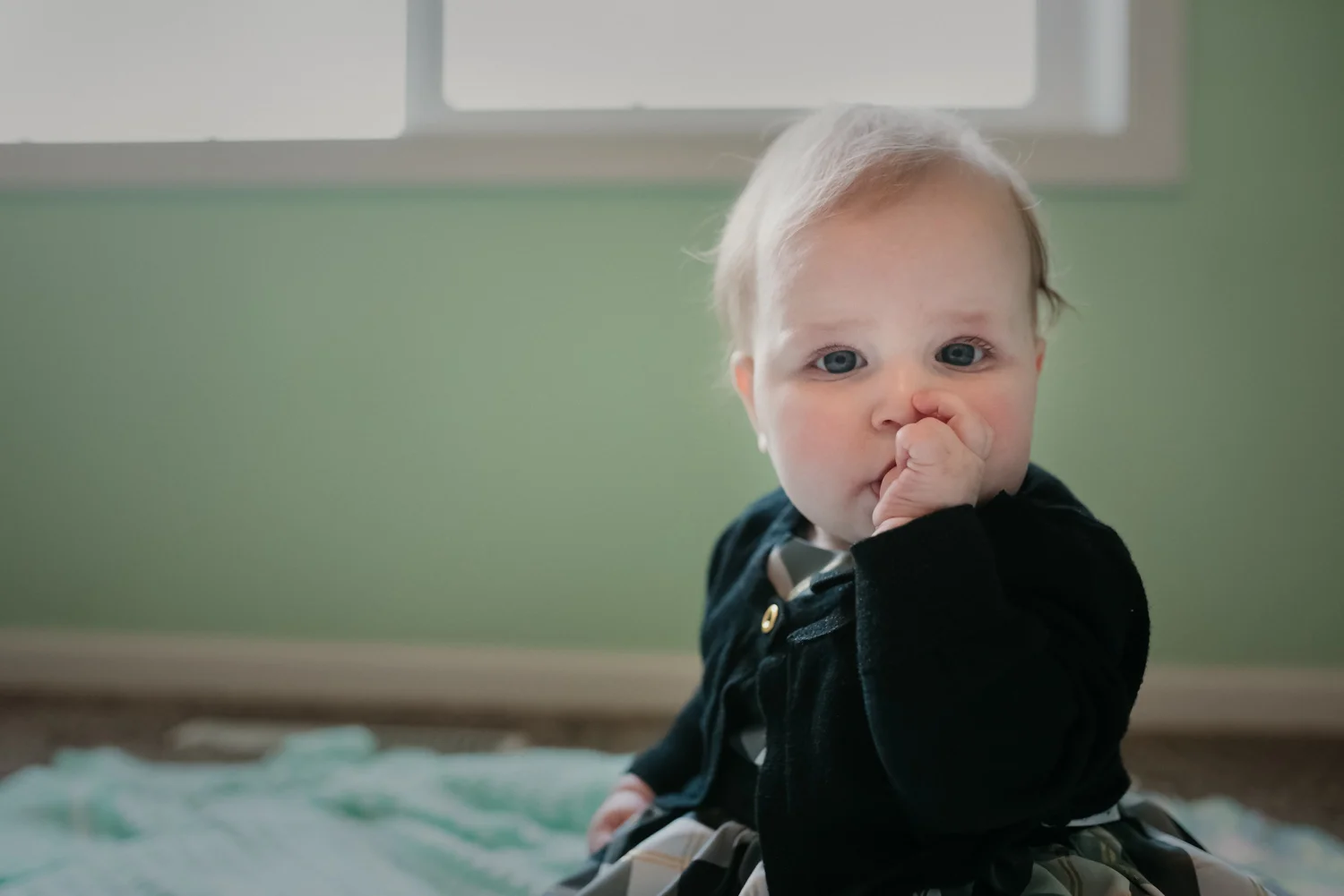 Baby sitting on the floor in her bedroom sucking her thumb.