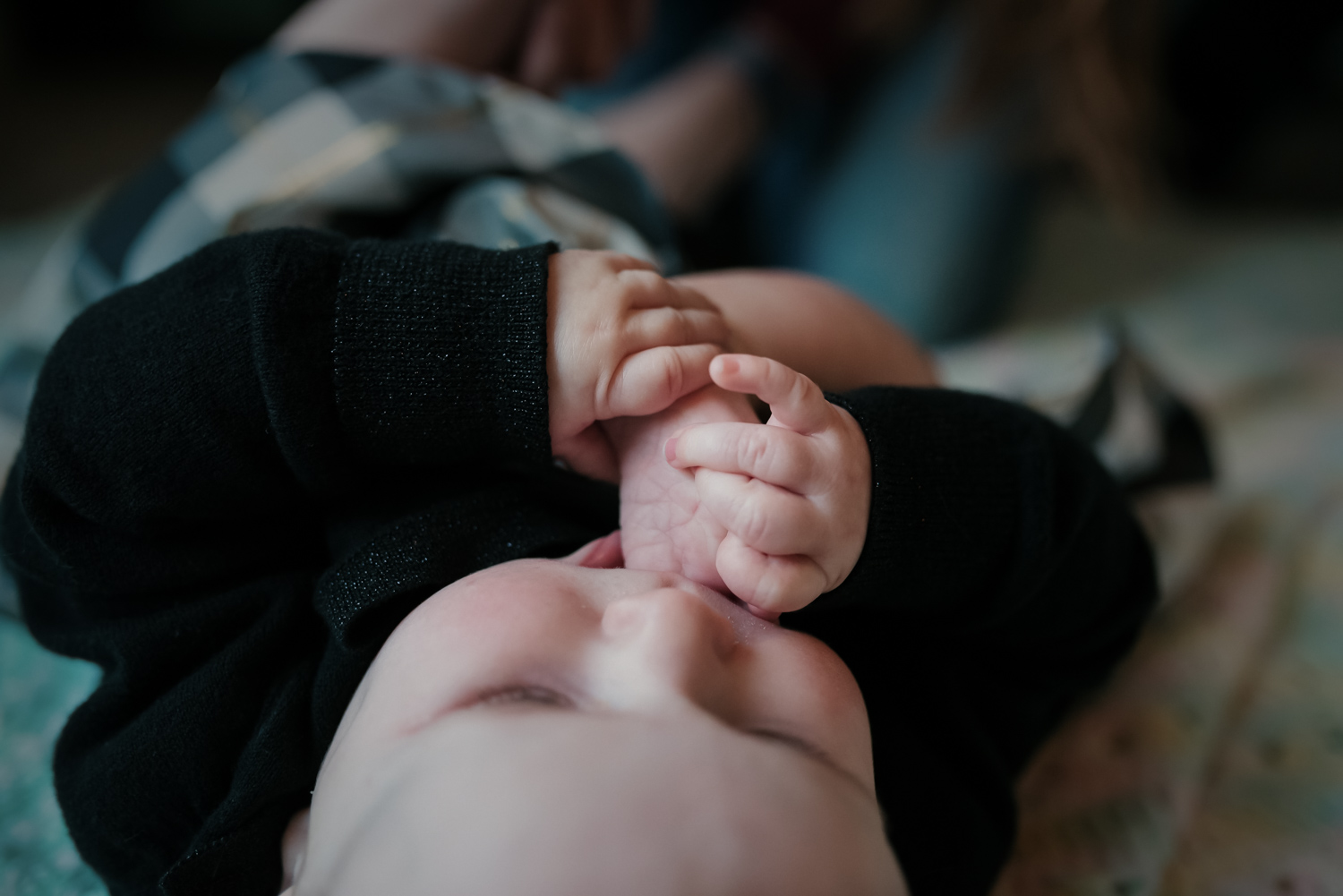 Baby holding her toes in her mouth while on her back.