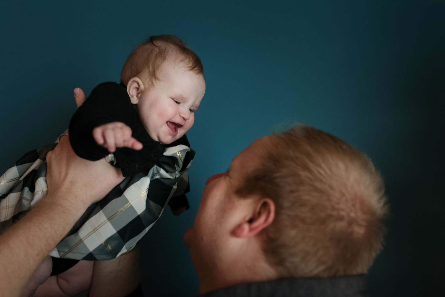 Dad holding baby up in front of him while baby smiles.