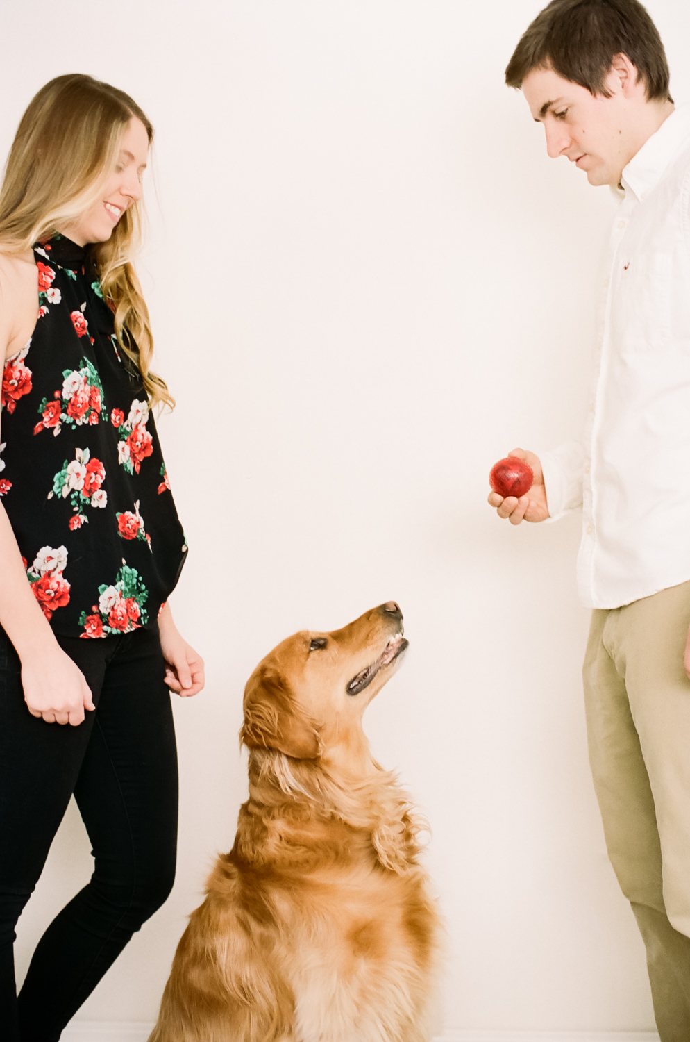 Portrait of a couple playing ball with their golden retriever.