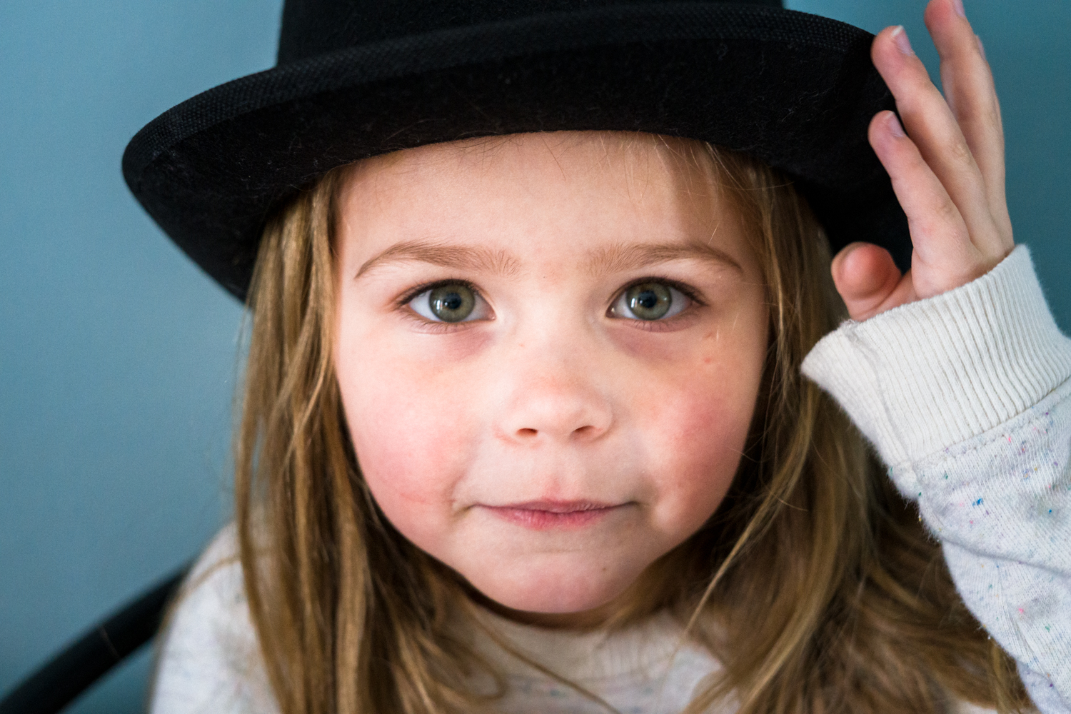 Portrait of a girl wearing a hat during dramactic play at daycare in Fargo with a playful smile on her face.