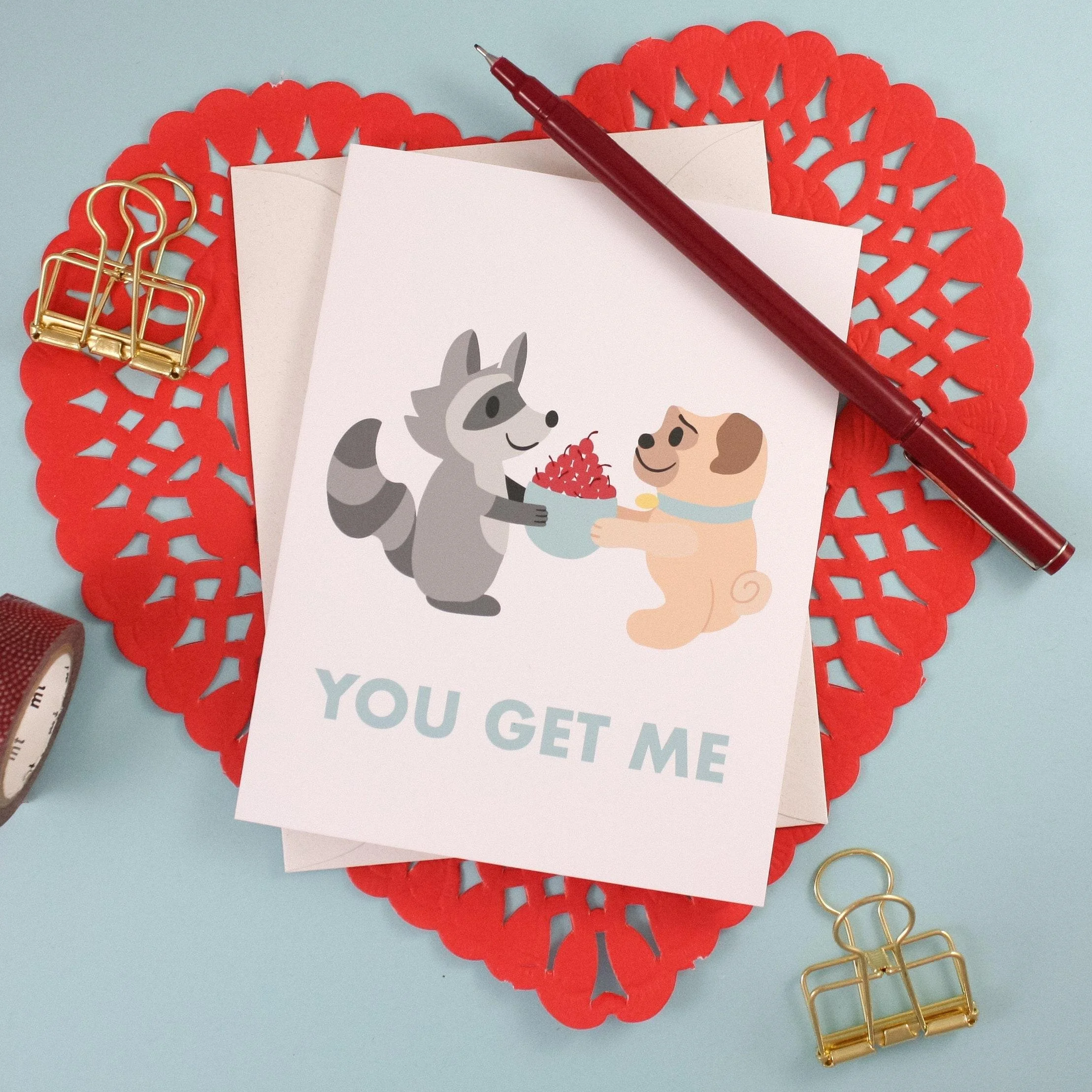 Greeting card with the message "You Get Me" below an illustration of a raccoon and a pug sharing a bowl of cherries