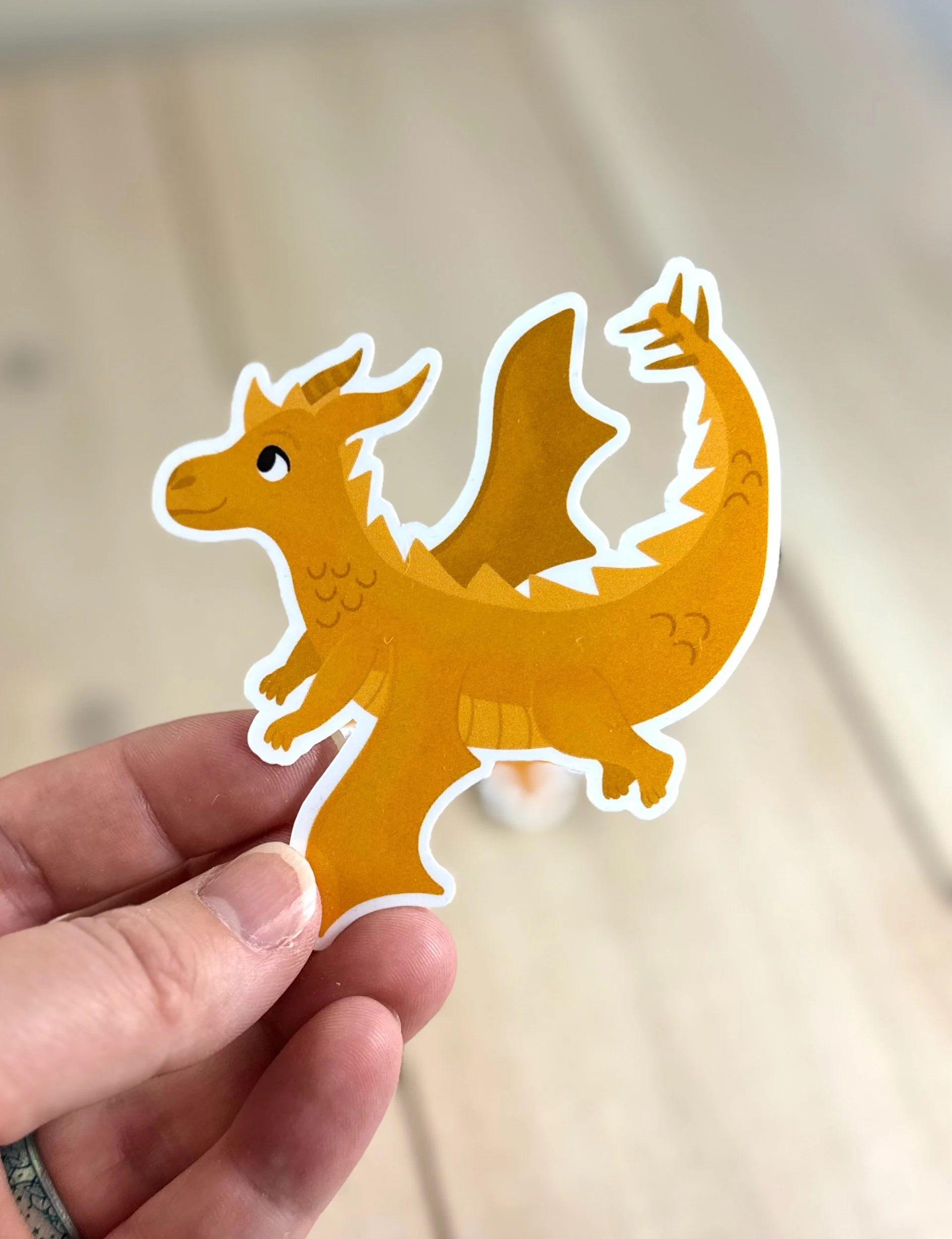 Golden dragon sticker being held in hand to show the textured detail of the hand drawn illustration