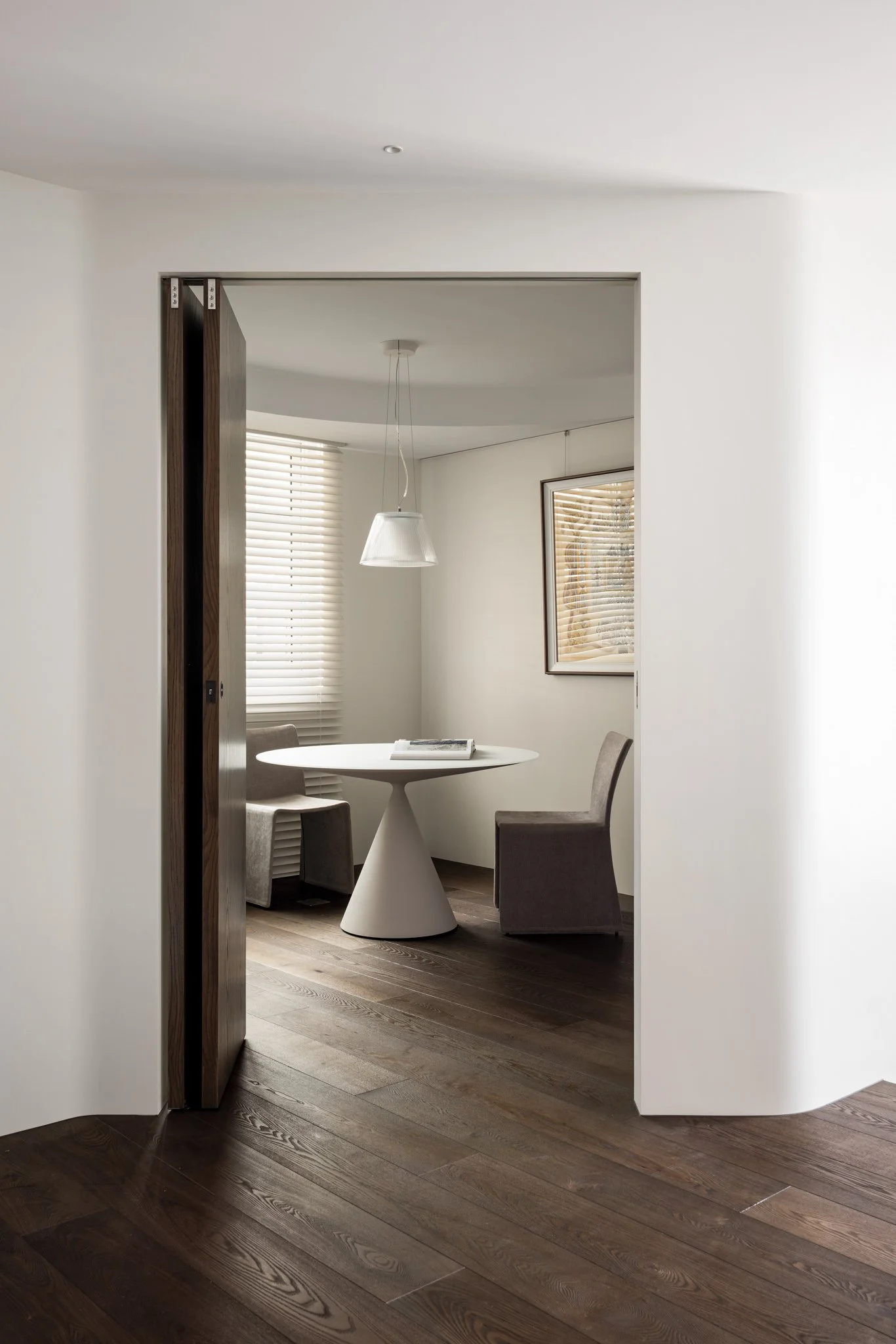 Home office of Pianist's with a Desalto Clay table and Flos Romeo pendant, framed by a softly curved opening and dark wood flooring.