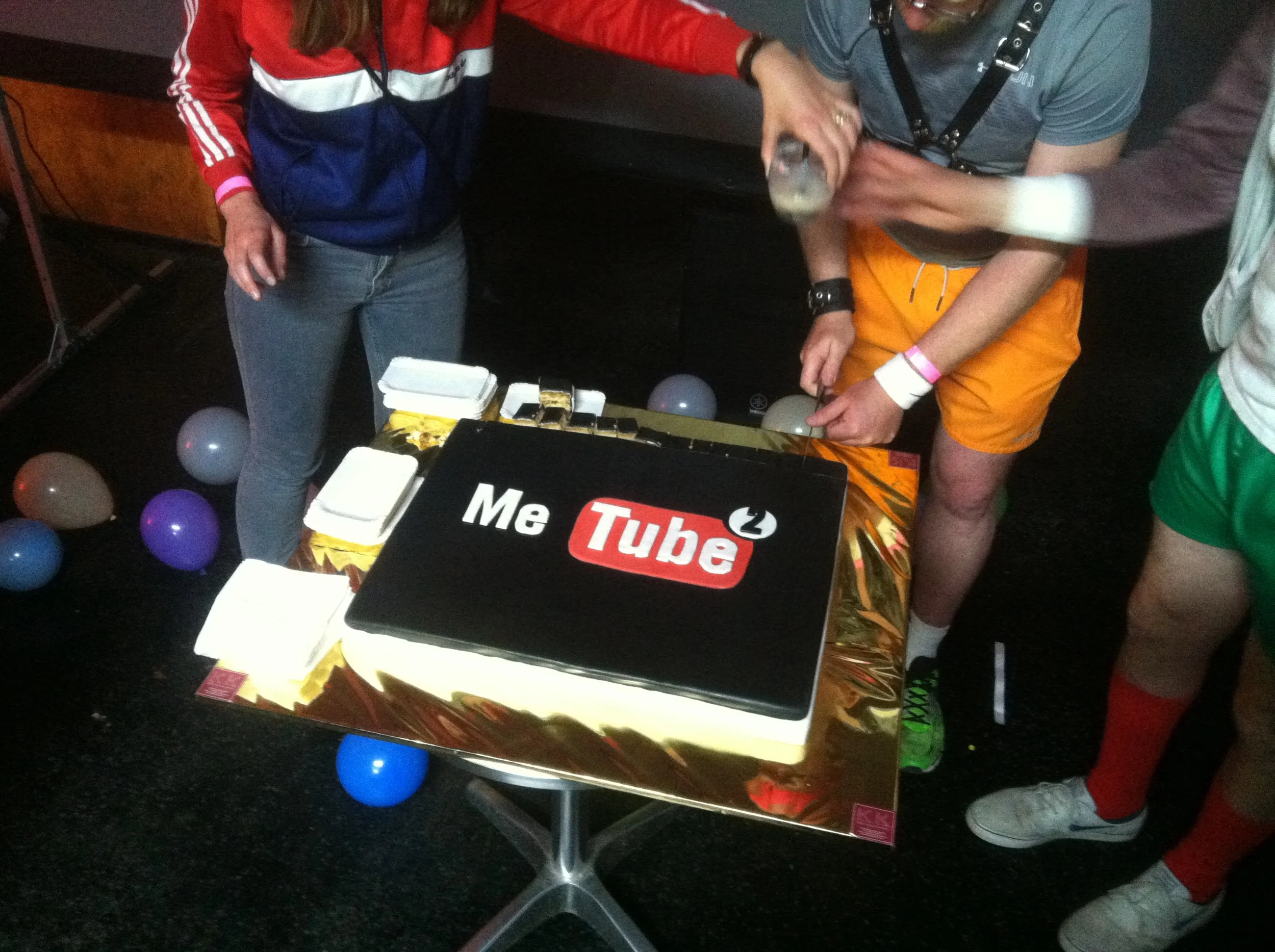 people in sport shorts cutting the official metube cake
