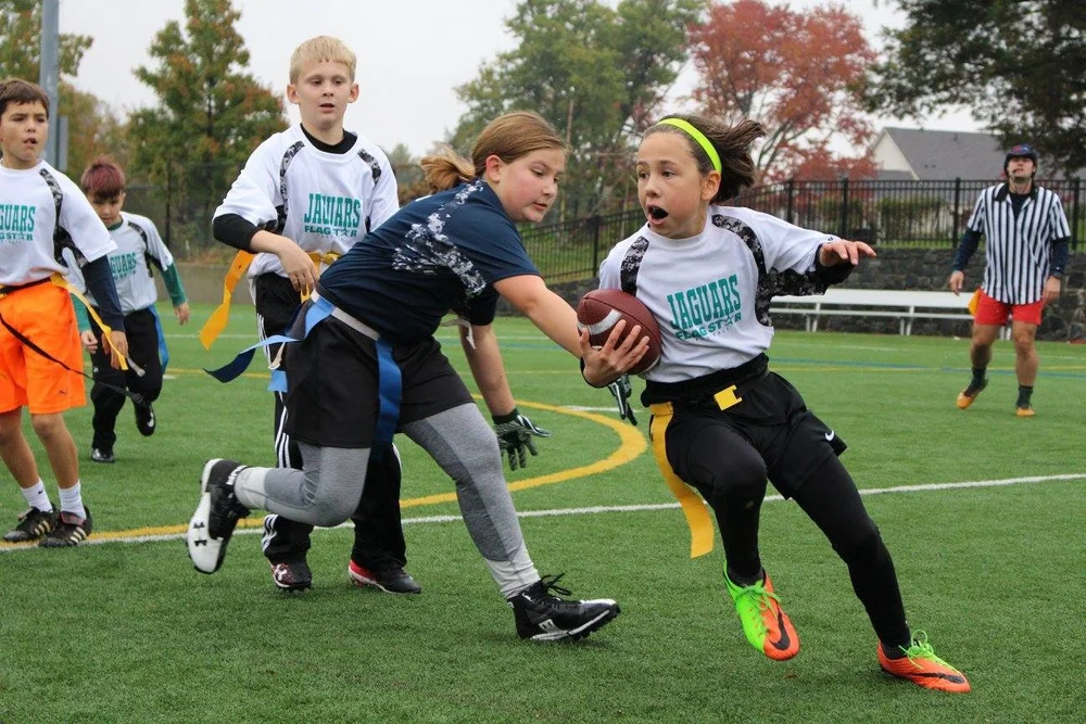Girls playing youth flag football on a turf field