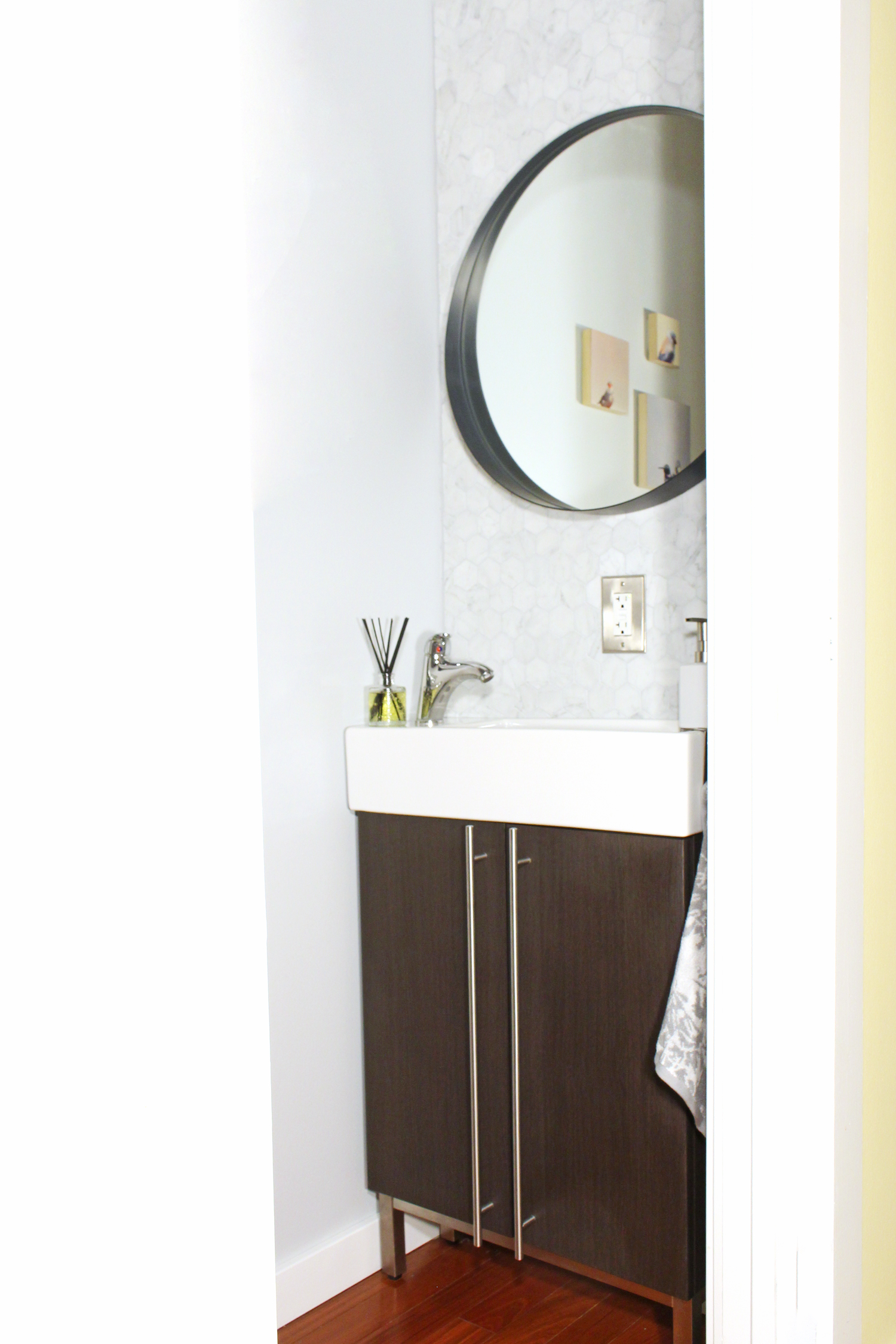 A small powder room makeover with marble hex tile and round mirror over a small, narrow vanity.