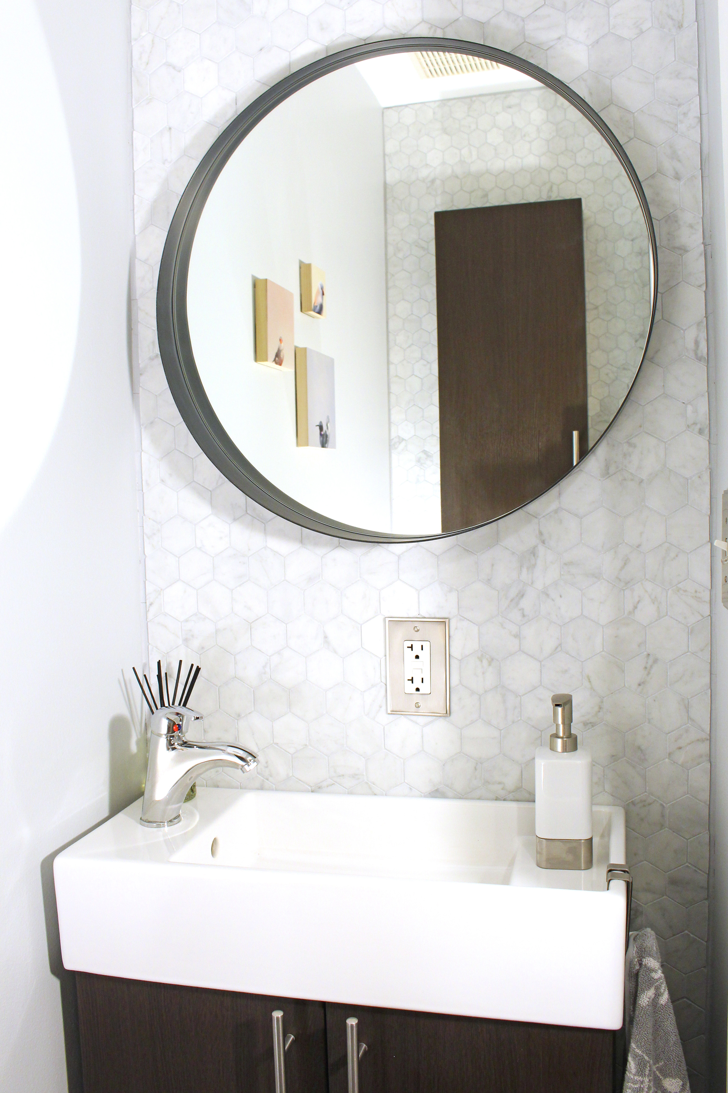 A small powder room makeover with marble hex tile and round mirror over a small, narrow vanity.