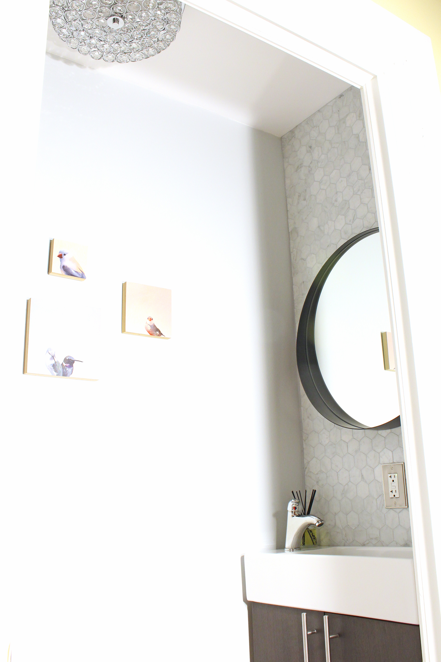 A small powder room makeover with marble hex tile and round mirror over a small, narrow vanity.