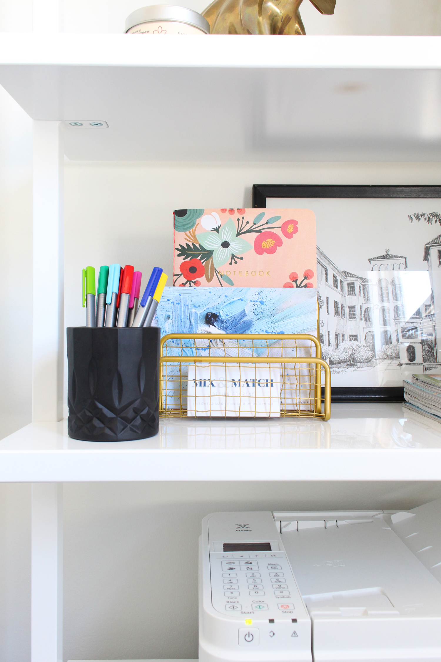 Office essentials and pretty pieces on bookshelf.