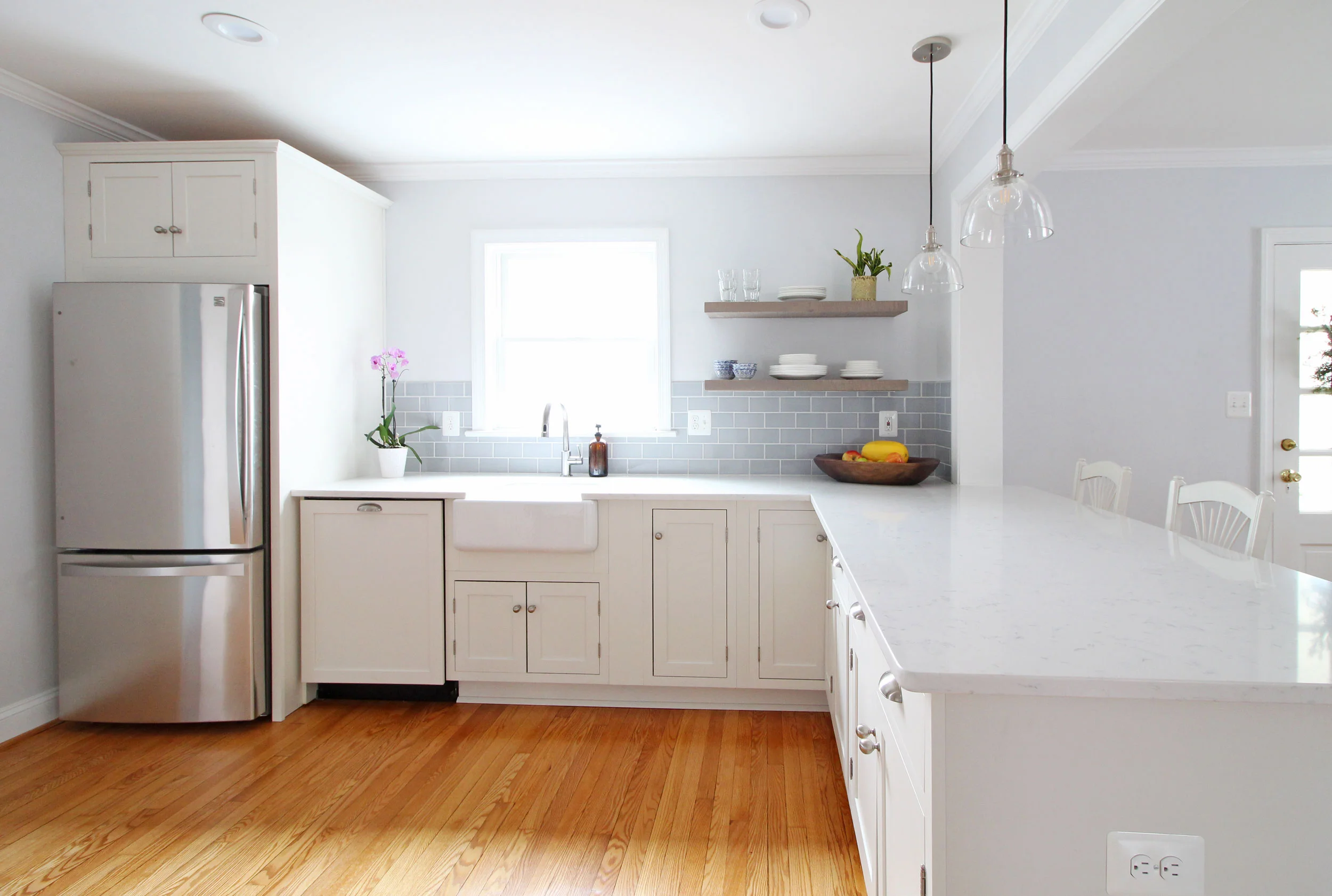 A stunning transitional farmhouse style white kitchen with inset cabinets opens up to the living room in this Virginia home. Open shelving is functional and stylish. You won't believe what this looked like before!