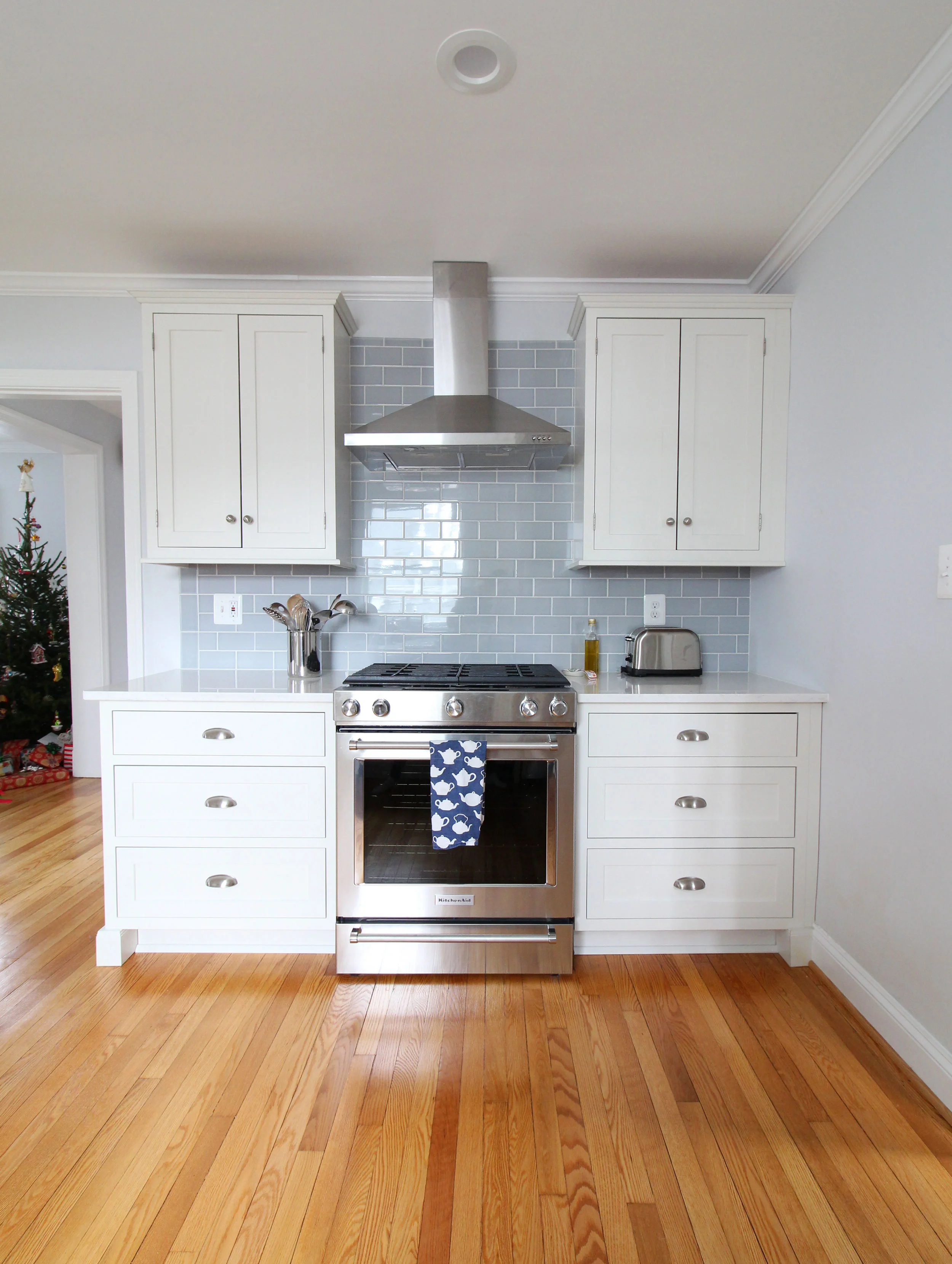 A stunning transitional farmhouse style white kitchen with inset cabinets opens up to the living room in this Virginia home. The range wall with blue glass subway tile is clean and fresh. You won't believe what this looked like before!