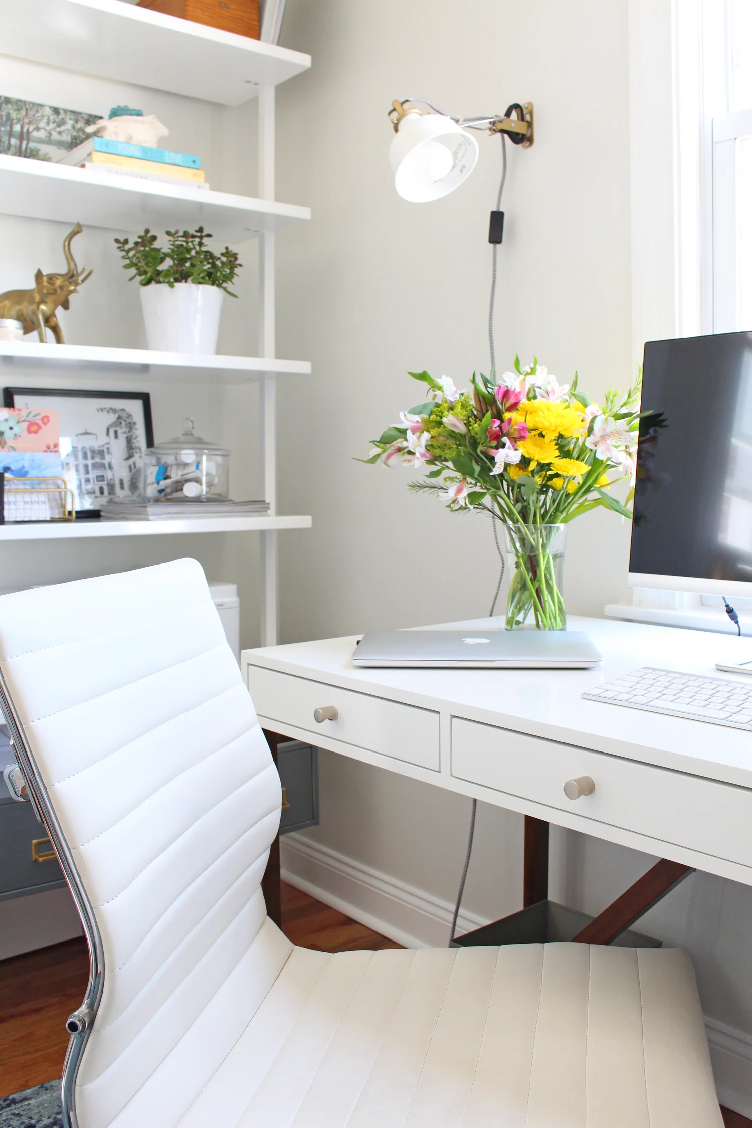 The light and bright home office of an interior designer has a white desk and an overdyed blue rug, as well as open bookshelves for storage.