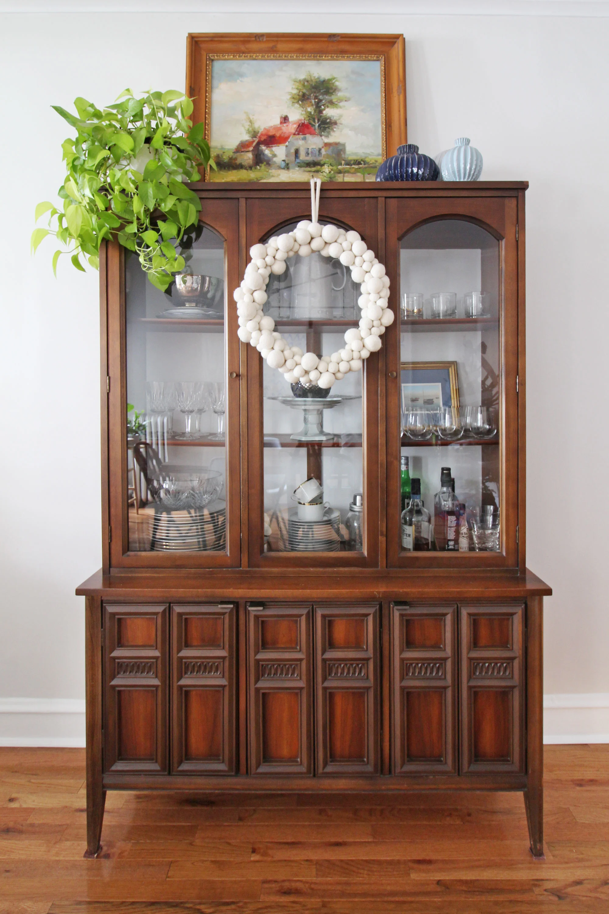 A simple way to add a little bit of Christmas cheer in your home is to hang a wreath in an unexpected spot. Here, I added a white felt ball wreath to our mid-century modern china cabinet. It’s the perfect touch of holiday spirit for our dining room. Christmas decorating can be simple and easy!