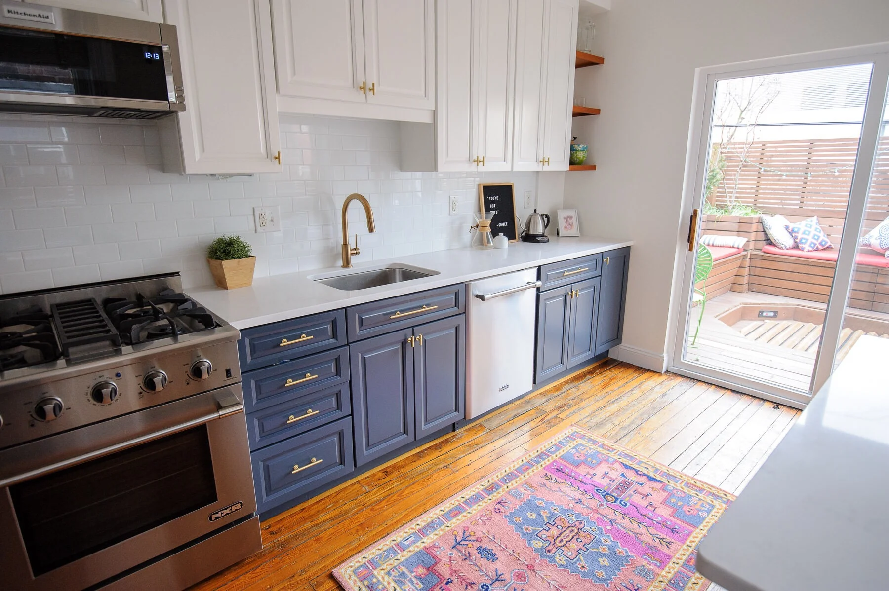 The after: a white, navy, and brass kitchen makeover in a Philadelphia row home. This kitchen got a serious refresh to give it a modern, clean, and cozy look. We chose Hale Navy for the lower cabinets, white subway tile, marble-like quartz countertops, and matte brass cabinet hardware. Designed by Mix & Match Design Company. Photos by Nate Photographic.