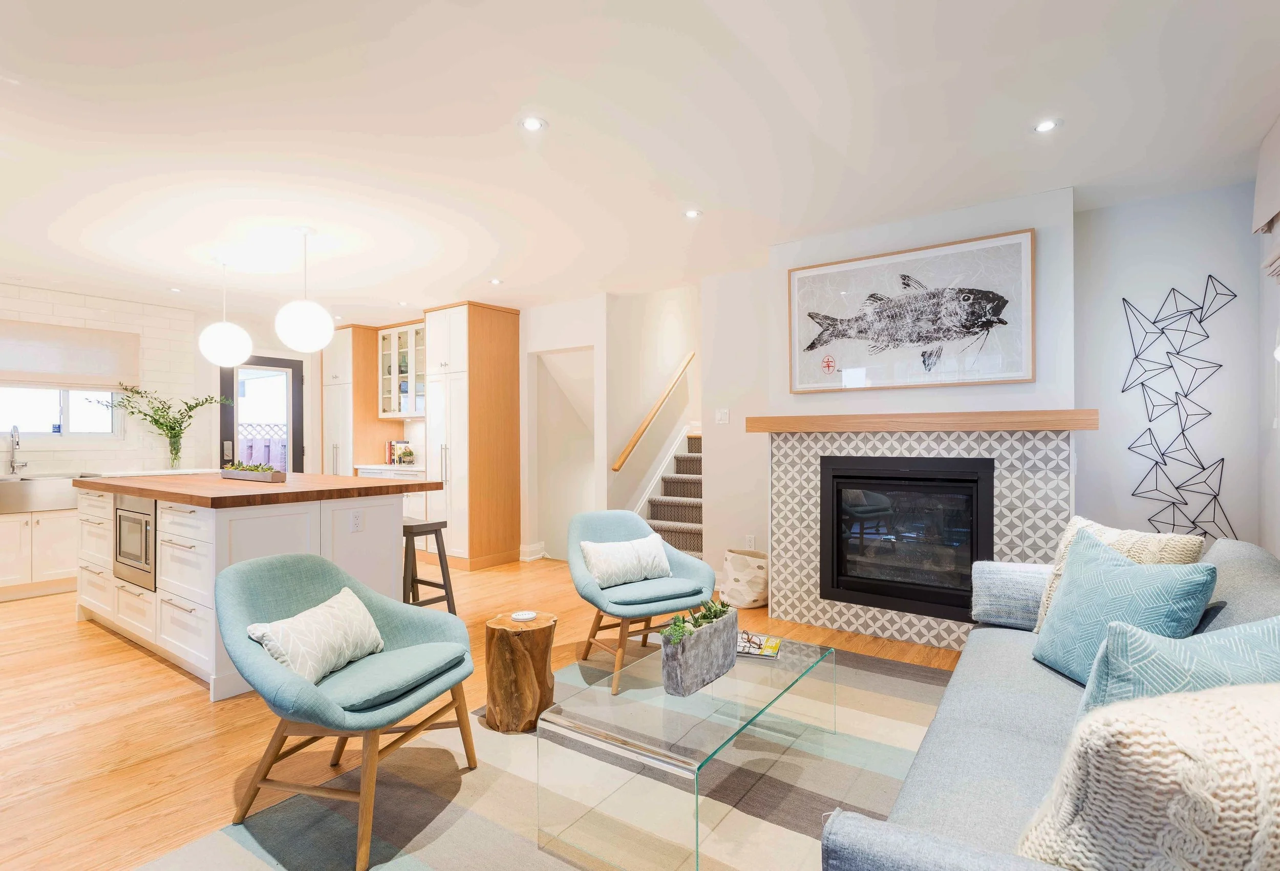 We designed the fireplace with a clean white boarder, modern tiles and a floating mantle. Hamilton Holmes also framed the art. This perspective also gives a view of the island and the side door storage with glass doors.