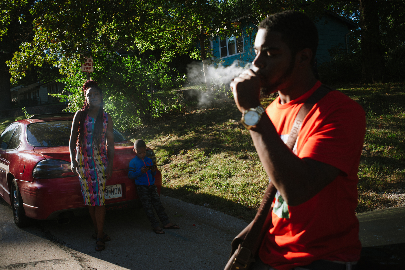A woman and her son watch as Meech smokes a blunt the night before the funeral of their friend Darnell Smith.