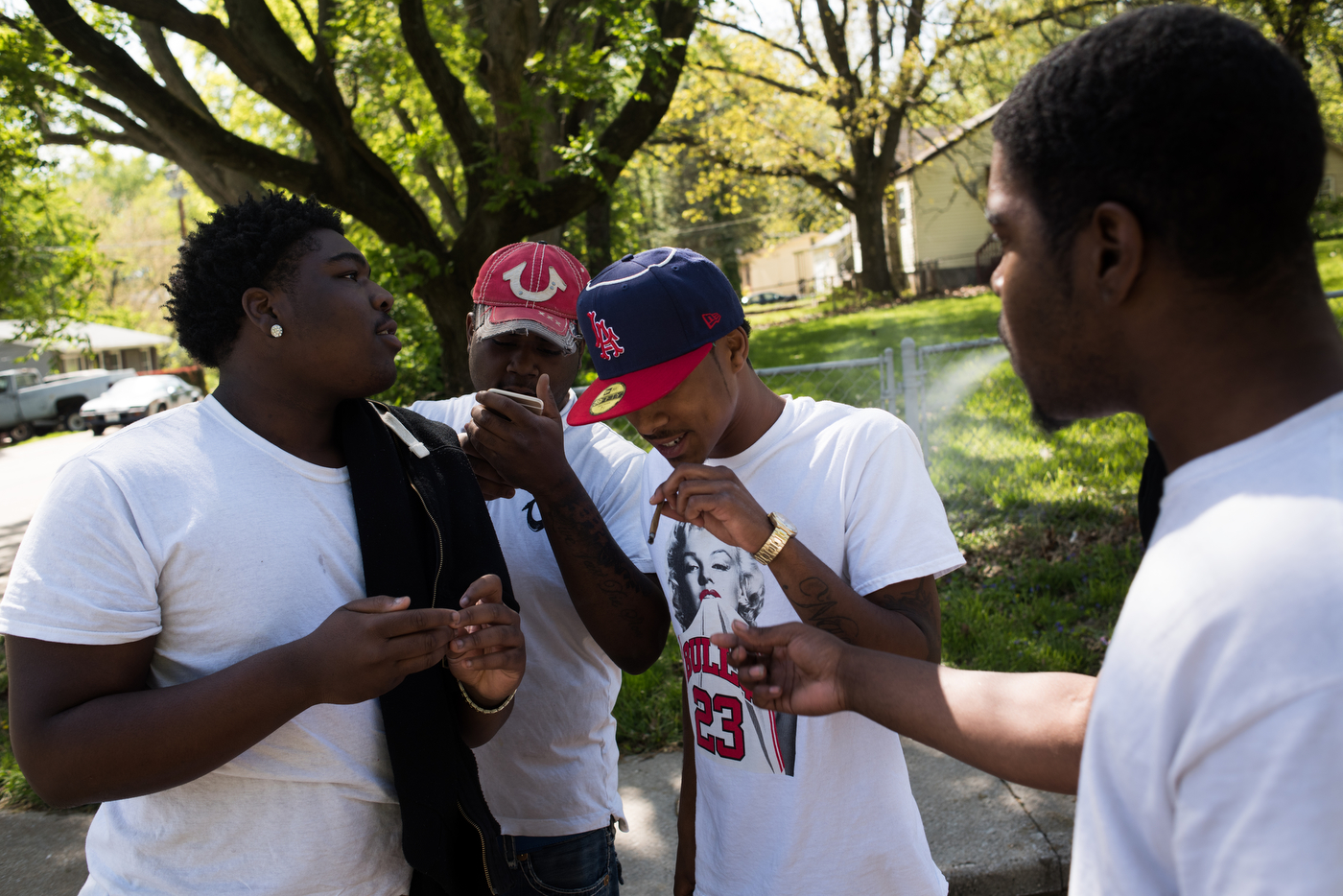TJ Banks goes to take a drag from a blunt while on a street corner in the Bermuda neighborhood in Ferguson, MO. After taking a semester off from community college to save money, TJ, his high school-aged neighbor Jorden (left) and their friends spend much of their time smoking and drinking.