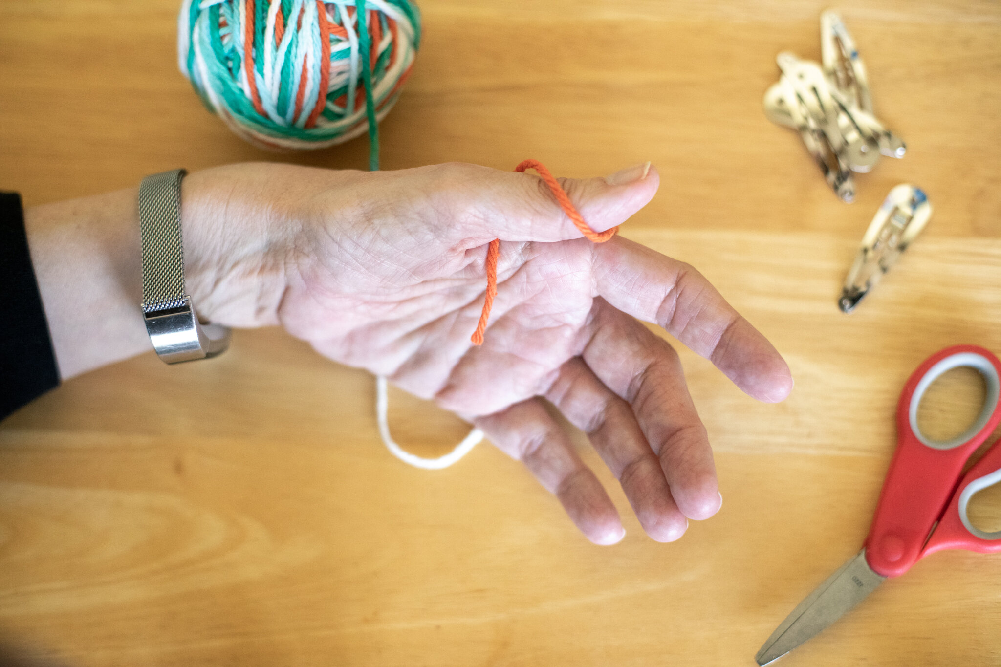  Loop the yarn around your thumb and behind your fingers. Keep pinching the “tail” of yarn so it doesn’t come loose. 