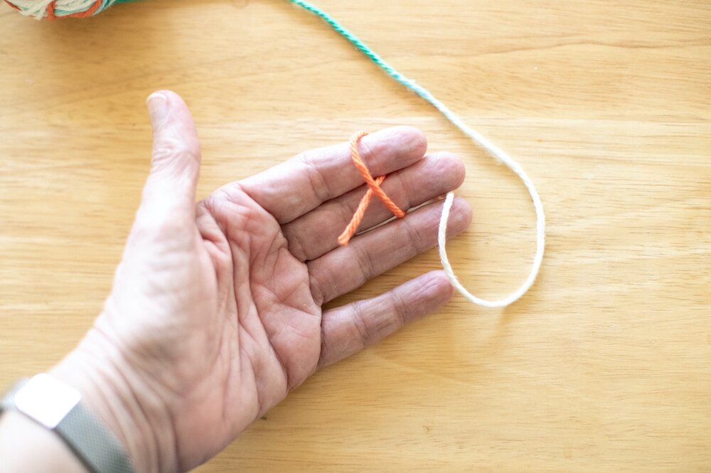  Hold/pinch the tail of the yarn between the first and second fingers of your less dominant hand (left hand if you write with your right hand). Loosely loop the yarn around your first two fingers. 
