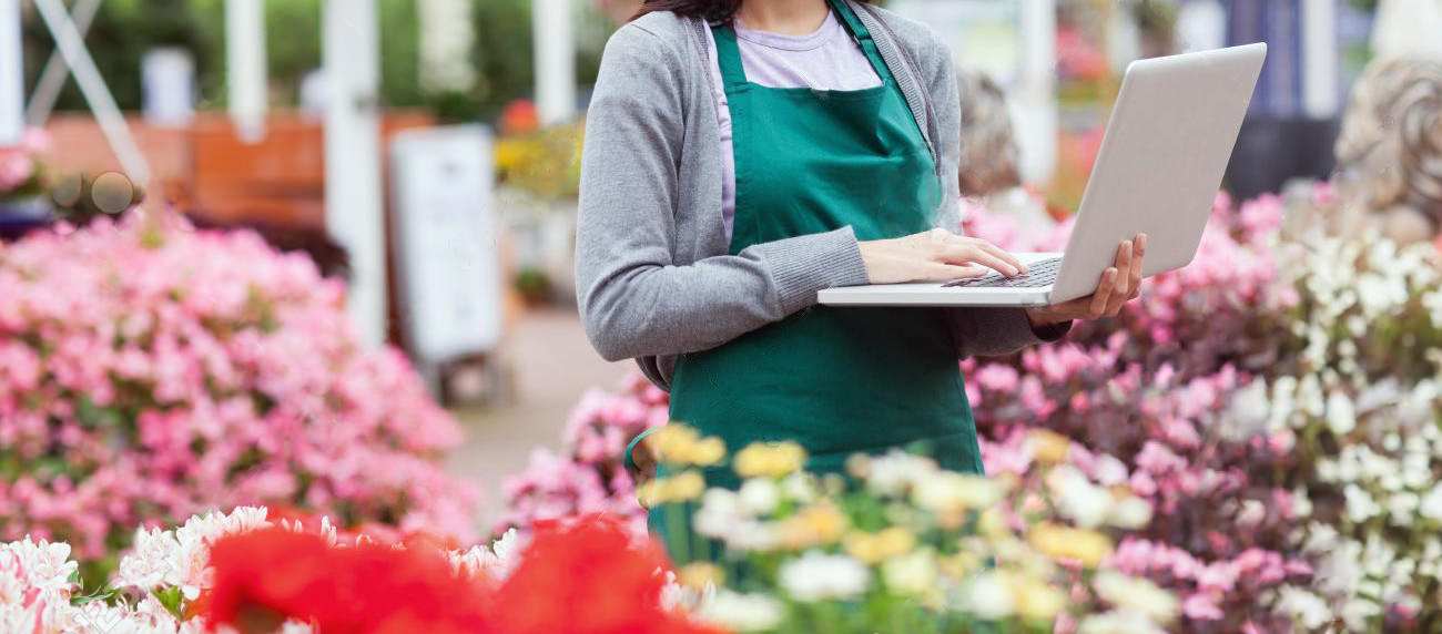 16068364-Woman-using-laptop-in-the-garden-center-while-smiling-Stock-Photo.jpg