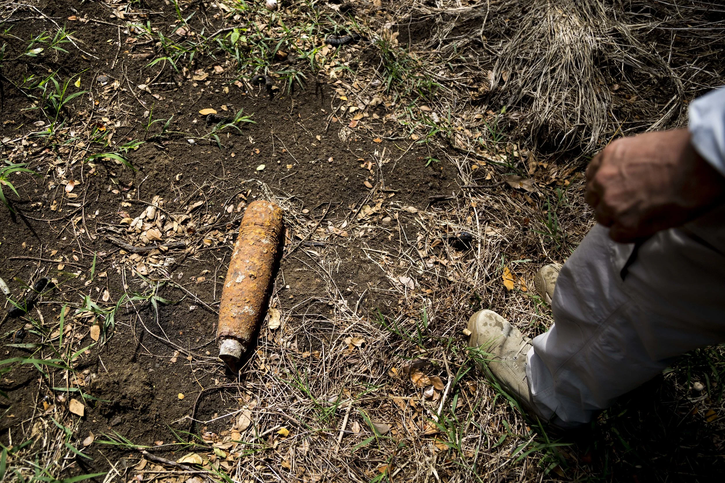  Golden West Humanitarian Foundation Project Manager, Paul Eldred looks down at his feet to where a 75mm high explosive projectile with a mechanical time fuse lies as he walks around Hells Point detonation range. Eldred warns not to touch this UXO as