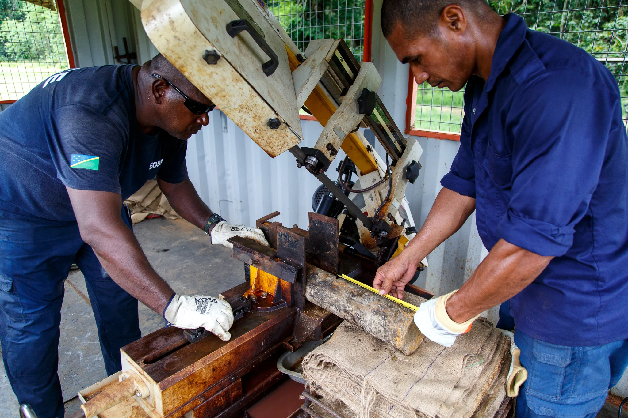  Sergeant Morris Ale and Police Constable Reinhard Alalo prepare a US 75mm high explosive projectile to be remotely cut by an automated cutting machine at the Hells Point Detonation Range in Honiara. The projectile must be precisely measured to ensur