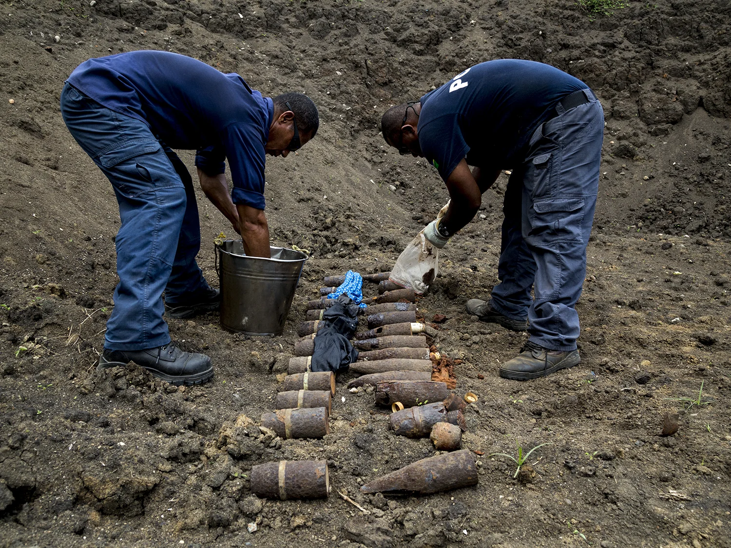  Police Constable Reinhard Alalo and Sergeant Morris Ale prepare the UXO for disposal in Hells Point, Honiara. The projectiles which have been carefully sawn open are placed in a deep dug-out in the earth and covered with diesel soaked rags, ready to