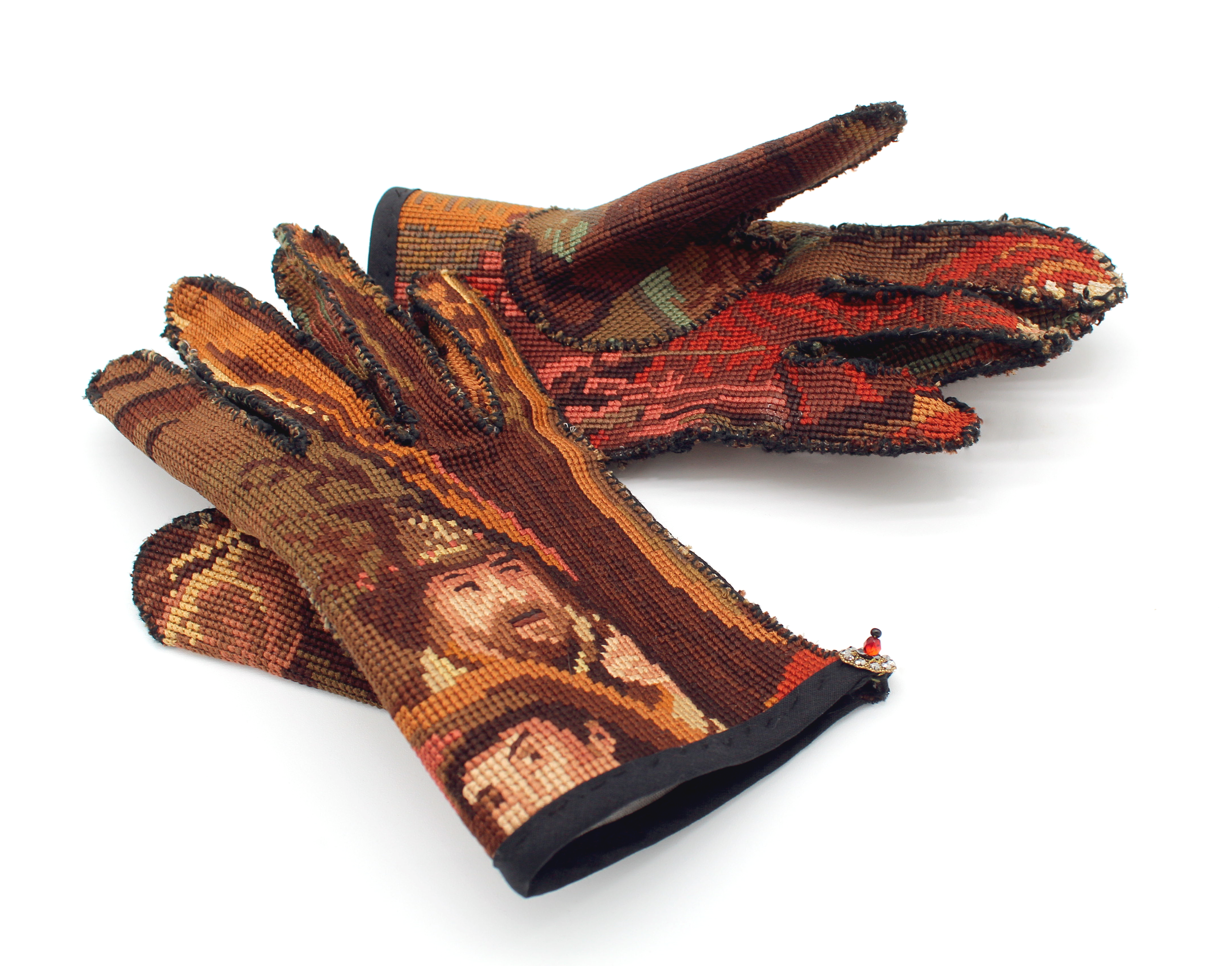 A pair of decorative, embroidered gloves with intricate patterns in warm colors including red, orange, and beige, against a white background.