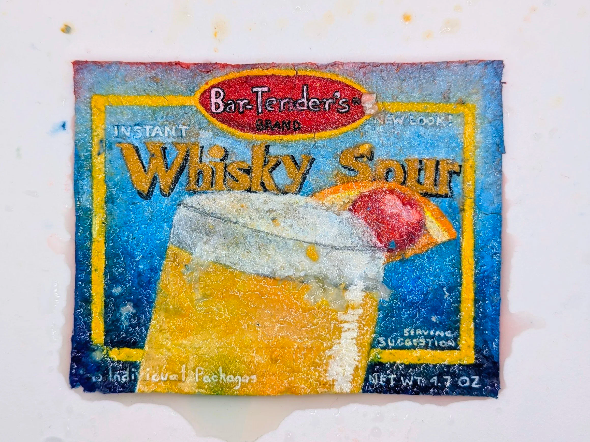 A colorful package of instant whiskey sour mix with a red and yellow logo at the top. The package features an illustration of a whiskey sour cocktail with an orange slice. The package is slightly worn and has a handwritten note at the bottom.