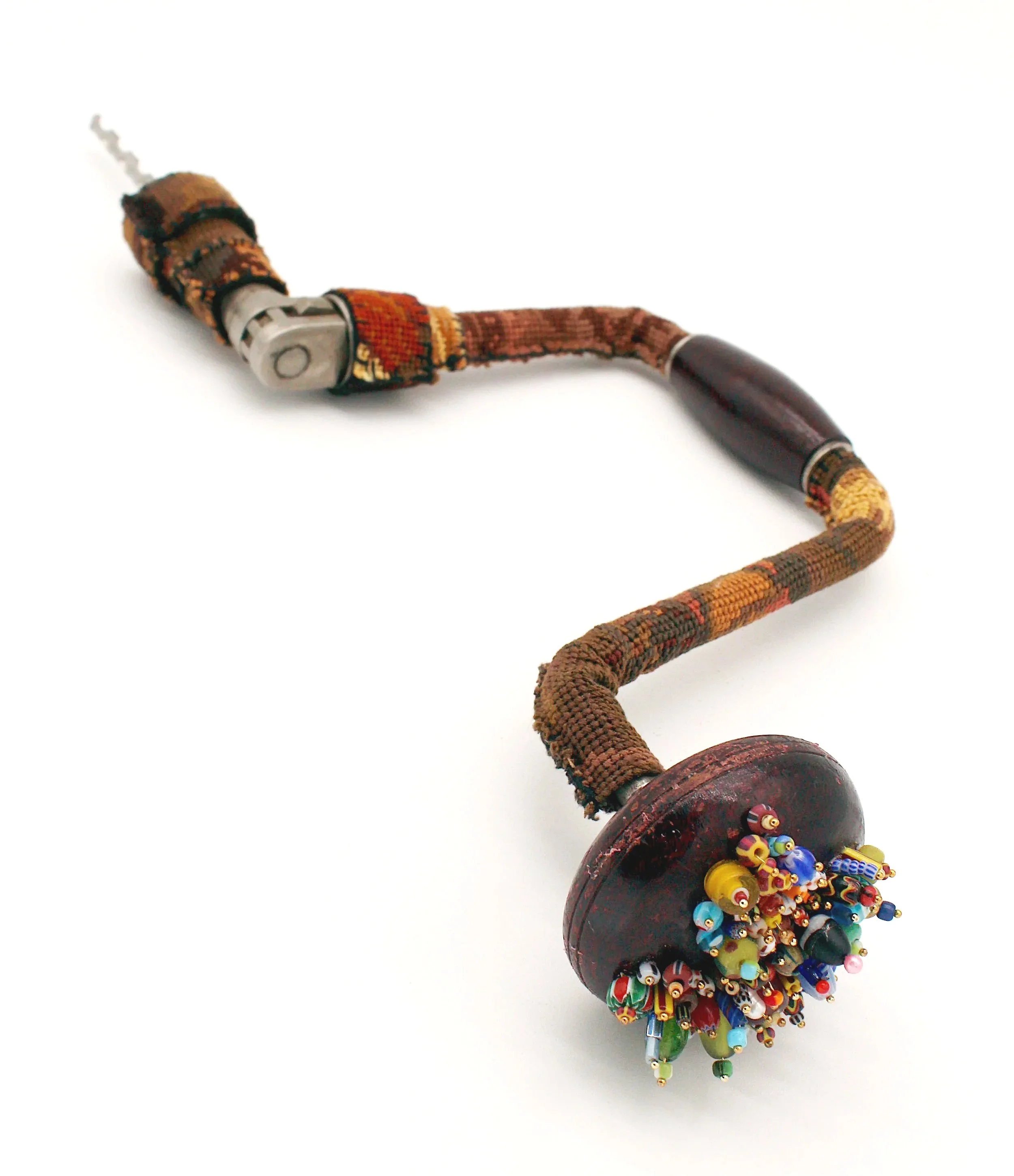 An antique hand drill covered in an earth tone cross-stitch with beads pinned into the wooden handle.