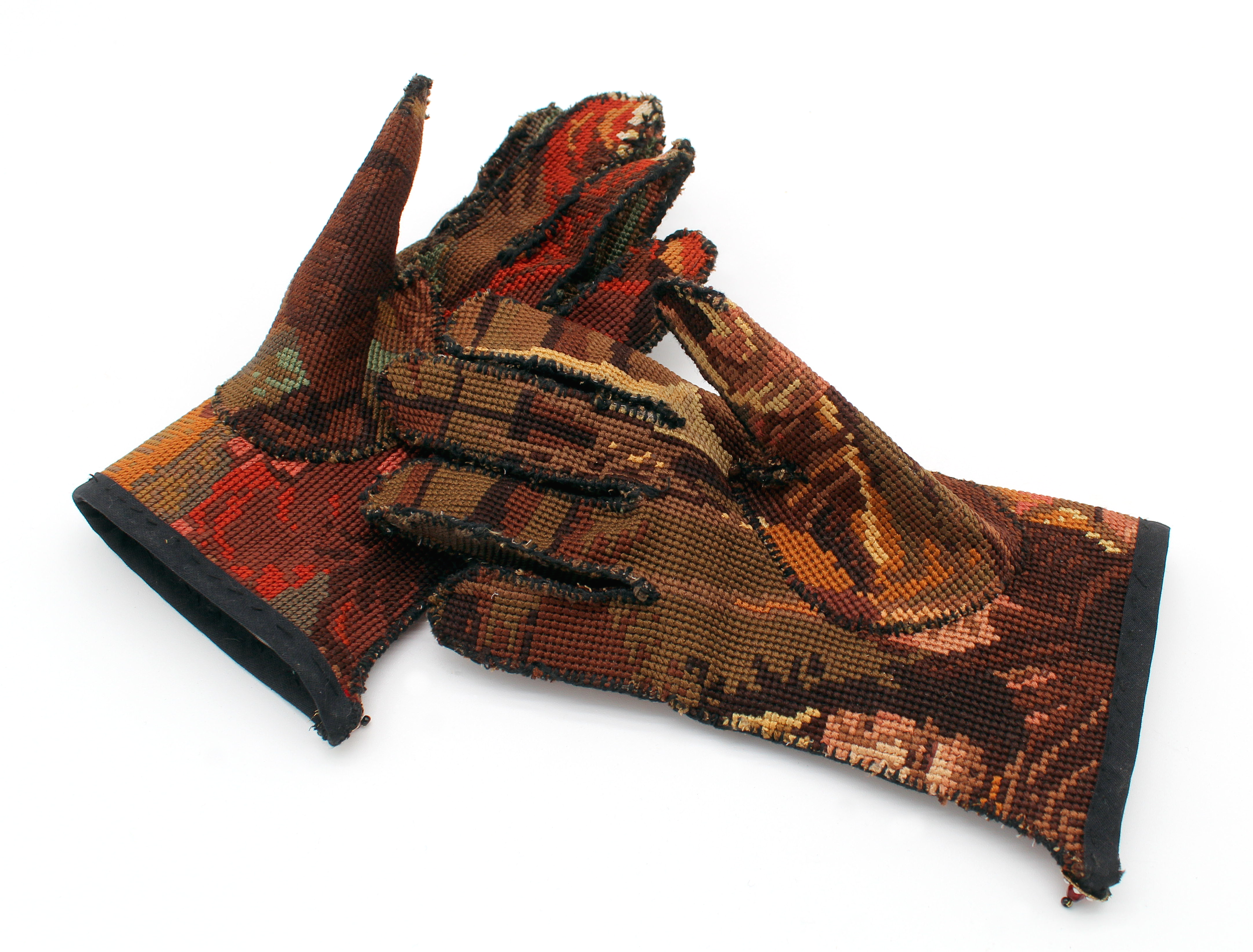 A pair of woven gloves with intricate patterns in red, orange, brown, and beige colors, laid flat on a plain white background.