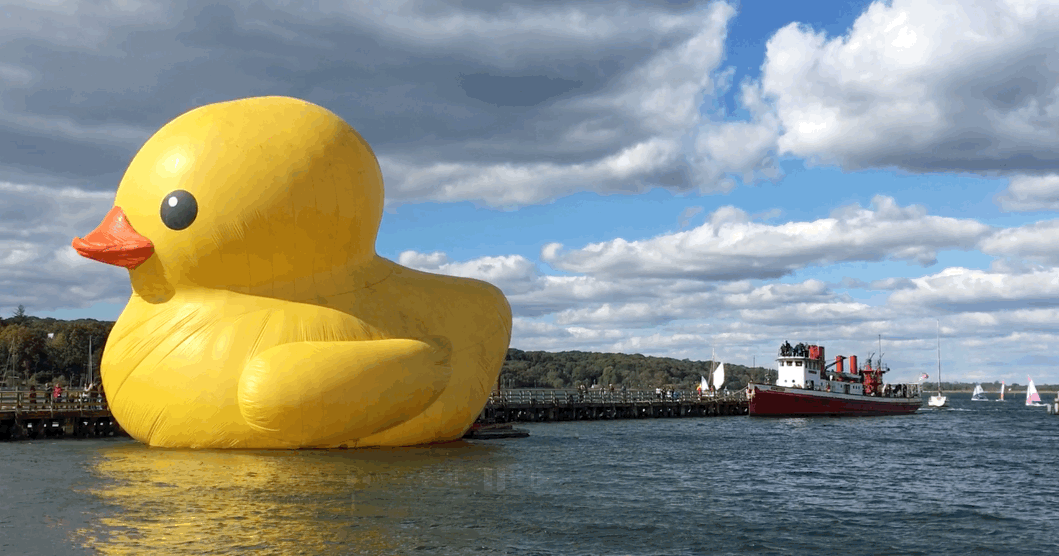 Lots to see here: big bobbing duck, red boat, boat race, clouds.