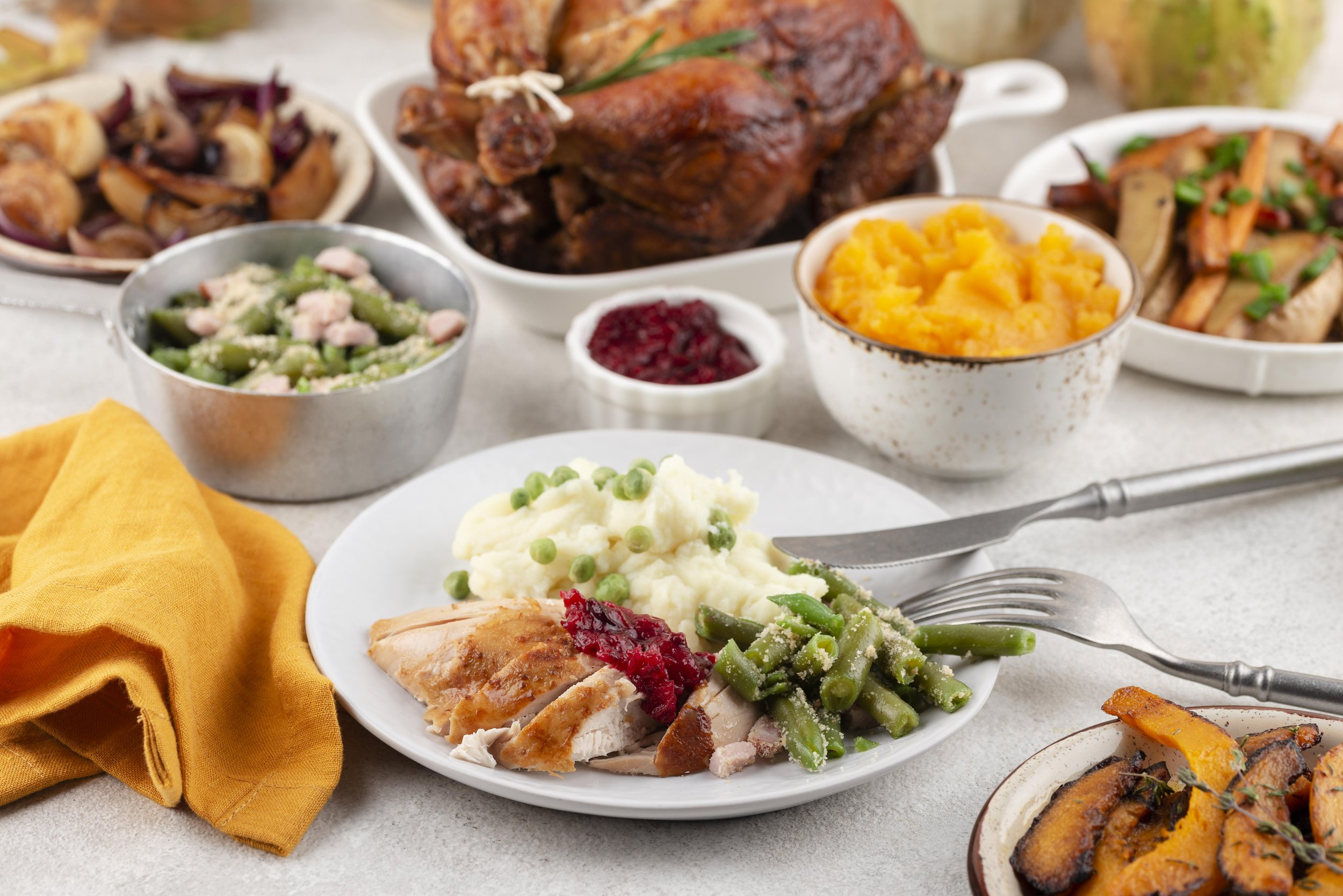 A Thanksgiving feast with turkey, mashed potatoes, green beans, cranberry sauce, stuffing, roasted vegetables, and other side dishes on a table.