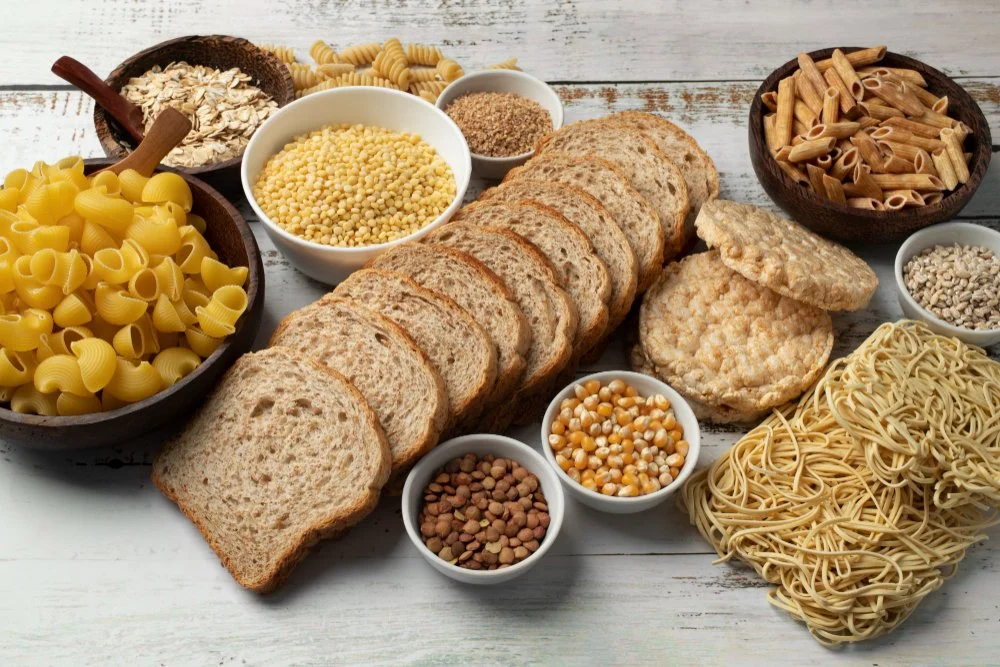 An assortment of bread and various types of pasta and grains on a white wooden surface.