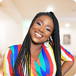A young woman with braided hair smiling, wearing a colorful striped top.