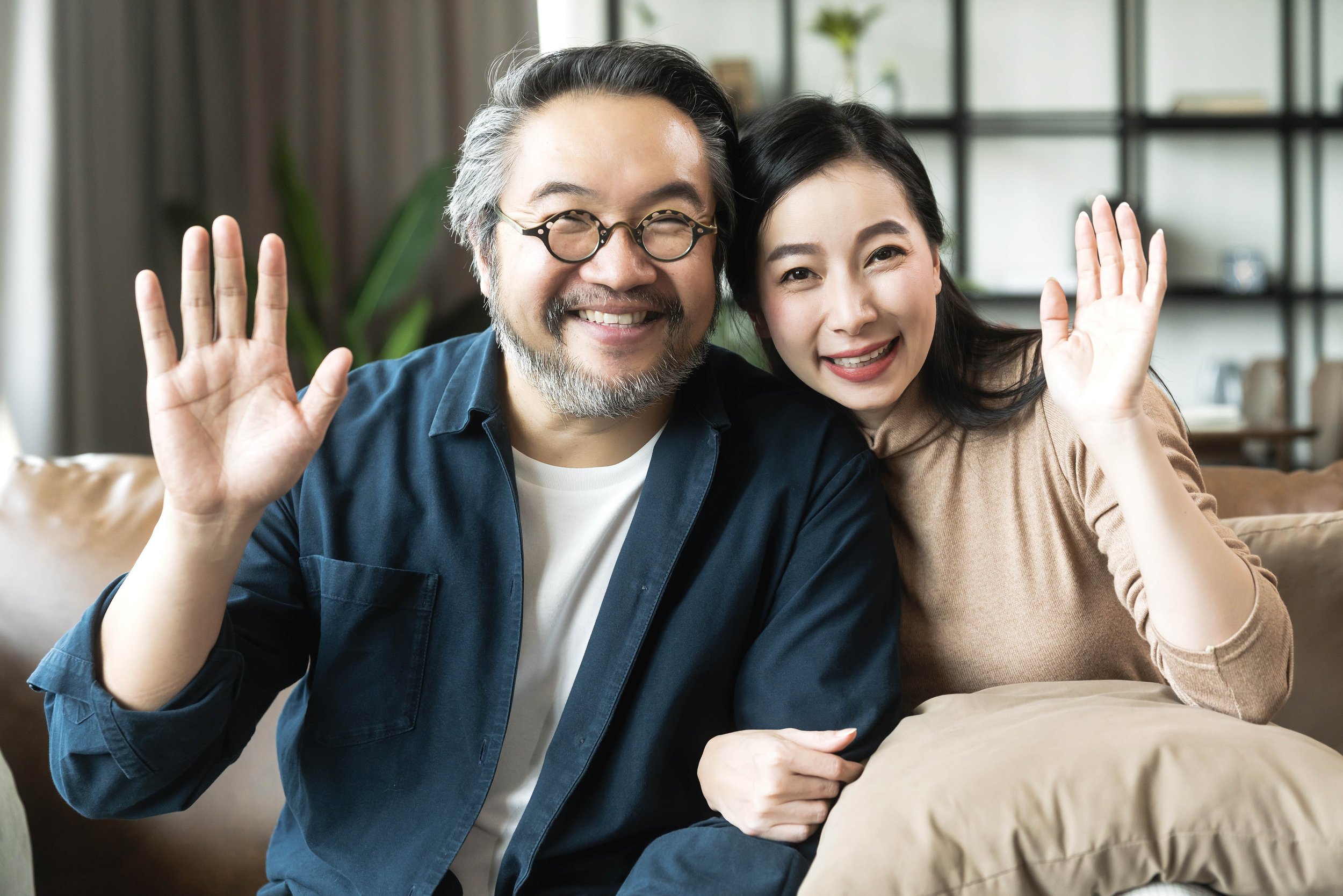 portrait-asian-mature-couple-sitting-smiling-living-room-wife-woman-hand-hold-husband-arm-from-look-camera-with-happiness-cheerful-safty-amd-insurance-family-concept-min.jpg