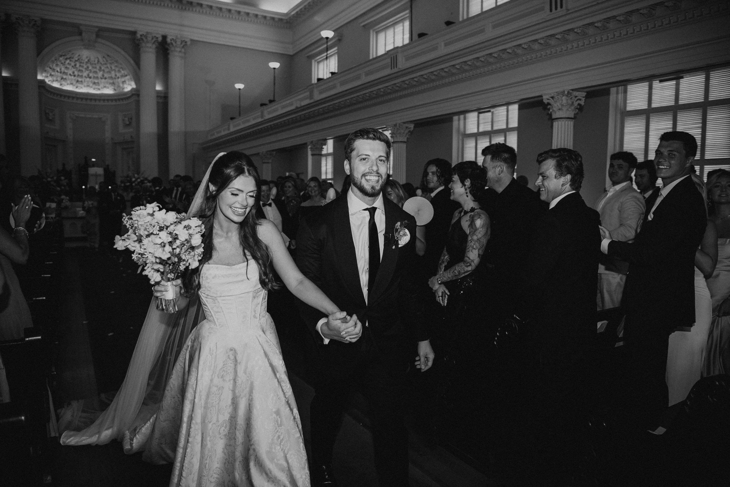 Black and white photo of Bride and groom smiling leaving the church after their ceremony