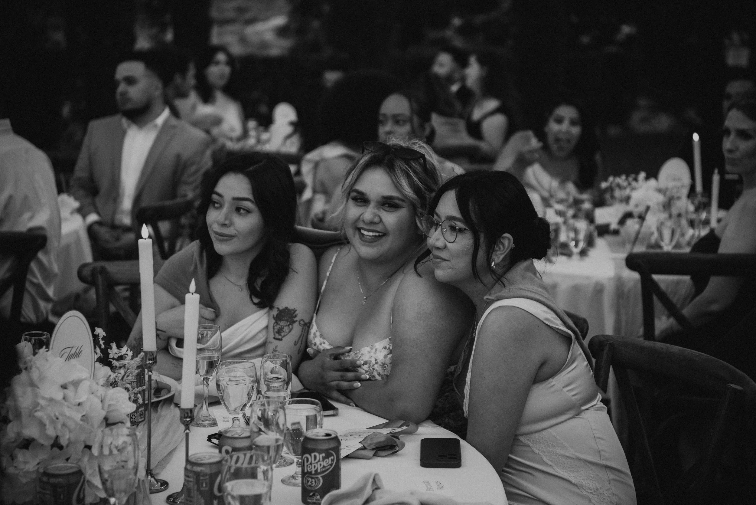 Black and white photo of 3 wedding guest sitting at a table as speeches are happening