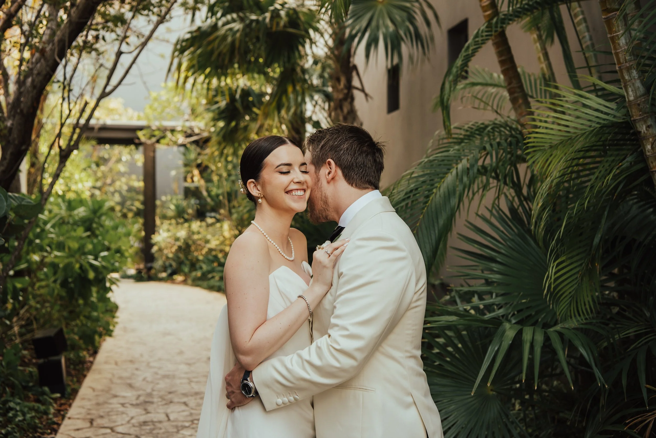 bride and groom hugging as groom whispers in her ear. Bride is smiling.