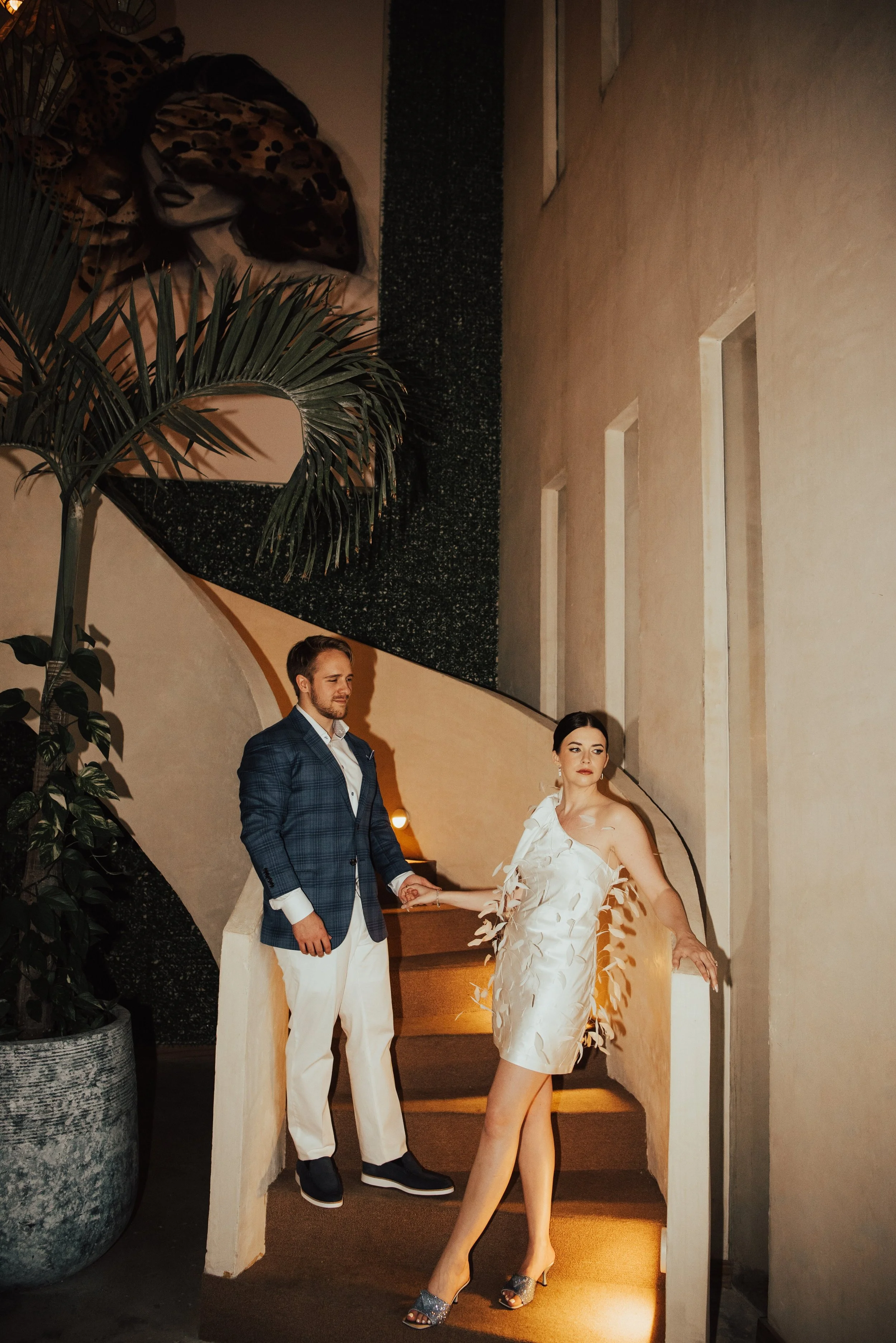 couple standing on rounding staircase. Couple is holding hand between them. Bride is looking off camera and groom is look at her