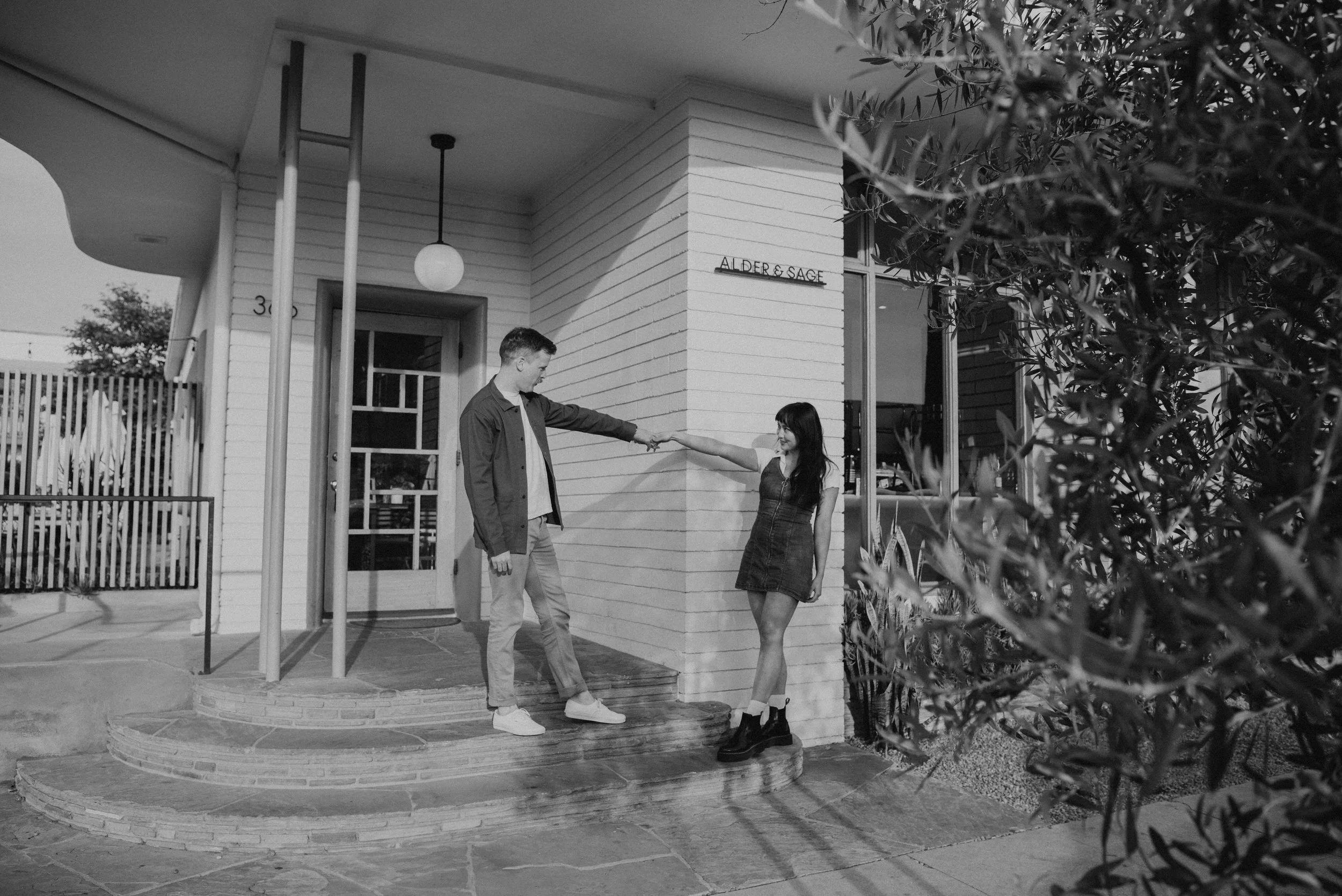 Couple standing on steps. guys on the step above the girl and they are holding hand with their arms stretch out between them