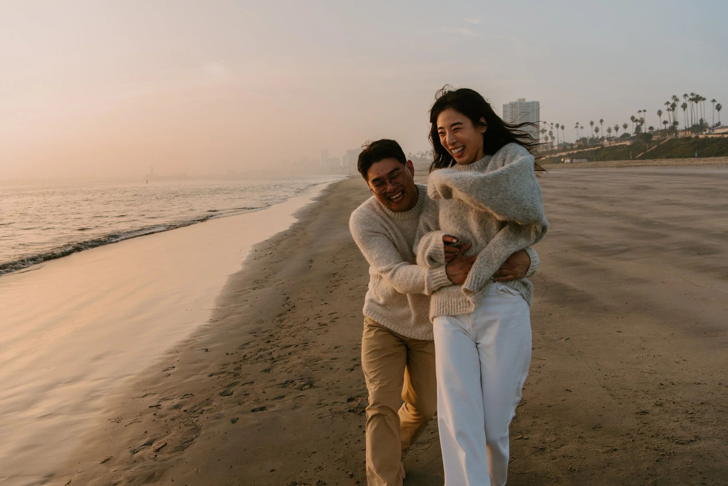 couple laughing on the beach as guy catches girl from behind