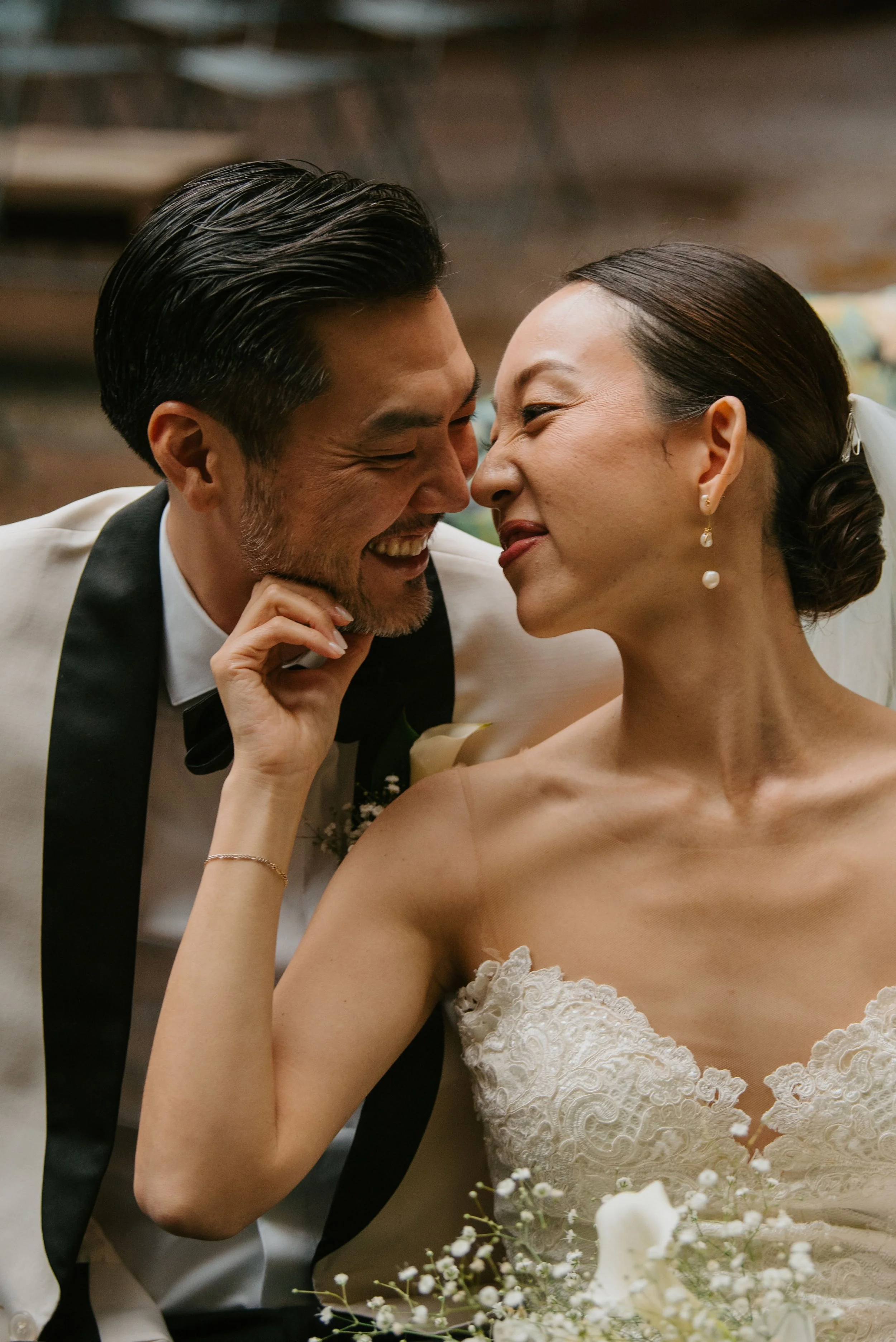 bride holding grooms face as they lean close and touch noses. Groom is smiling and Bride is scrunching her nose.