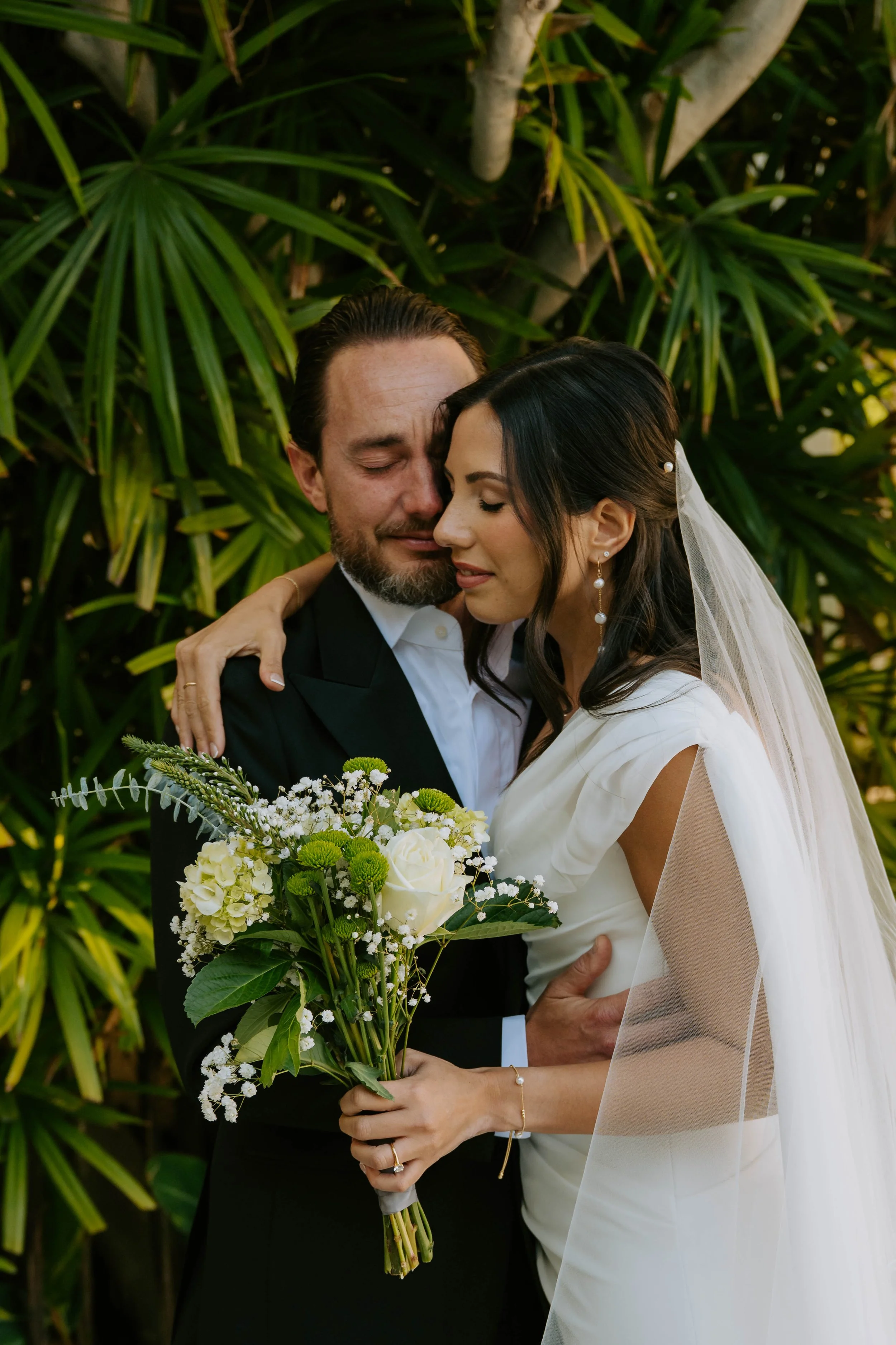 Bride and Groom share an emotional hug in front of plants