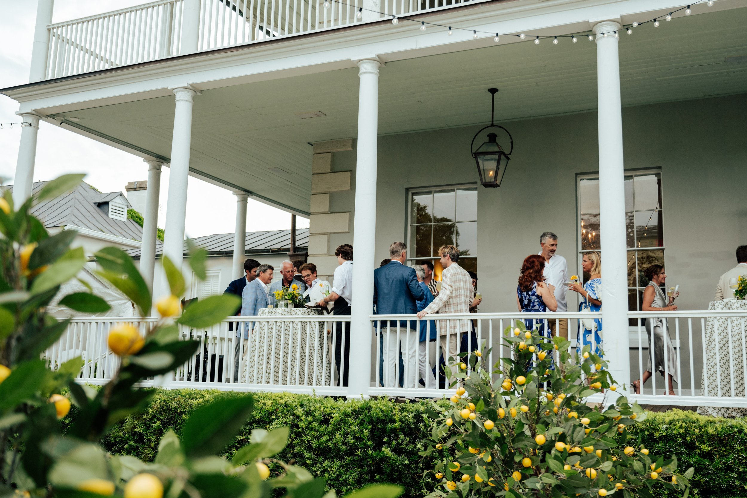 Wide shot of guest mingling on the wrap around porch of a house in Charleston South Carolina