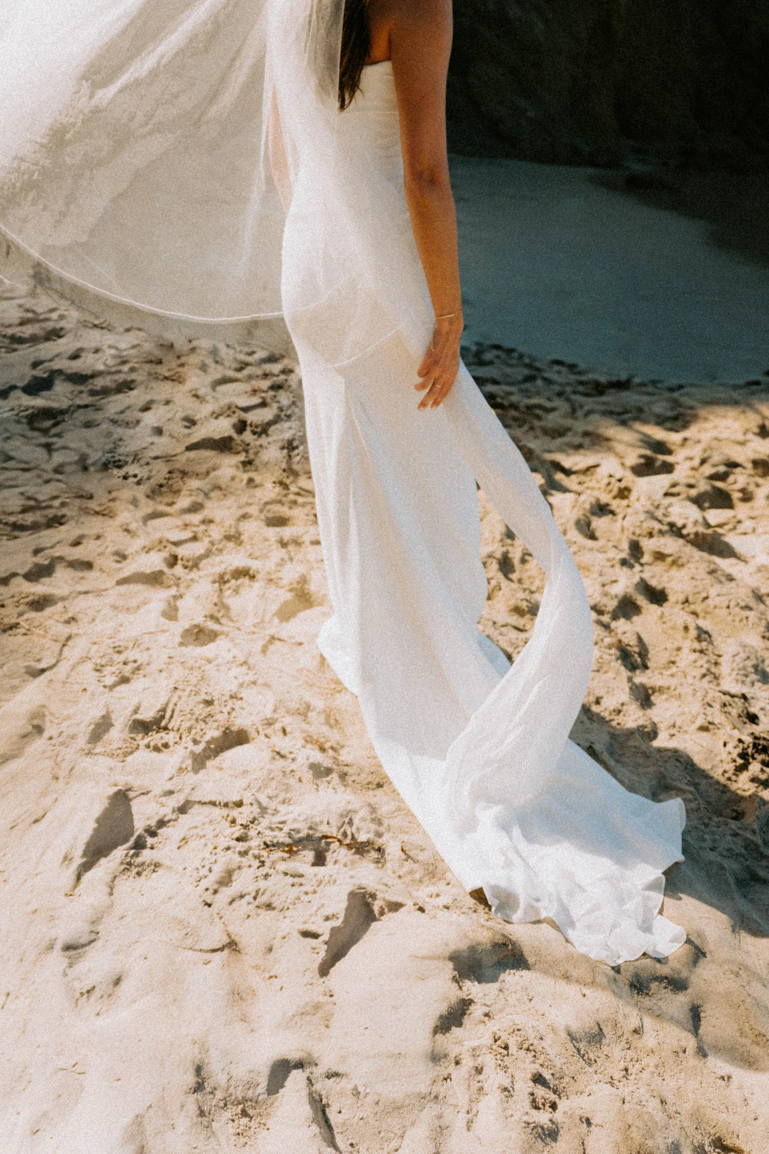bride standing on the beach with her dress blowing in the wind