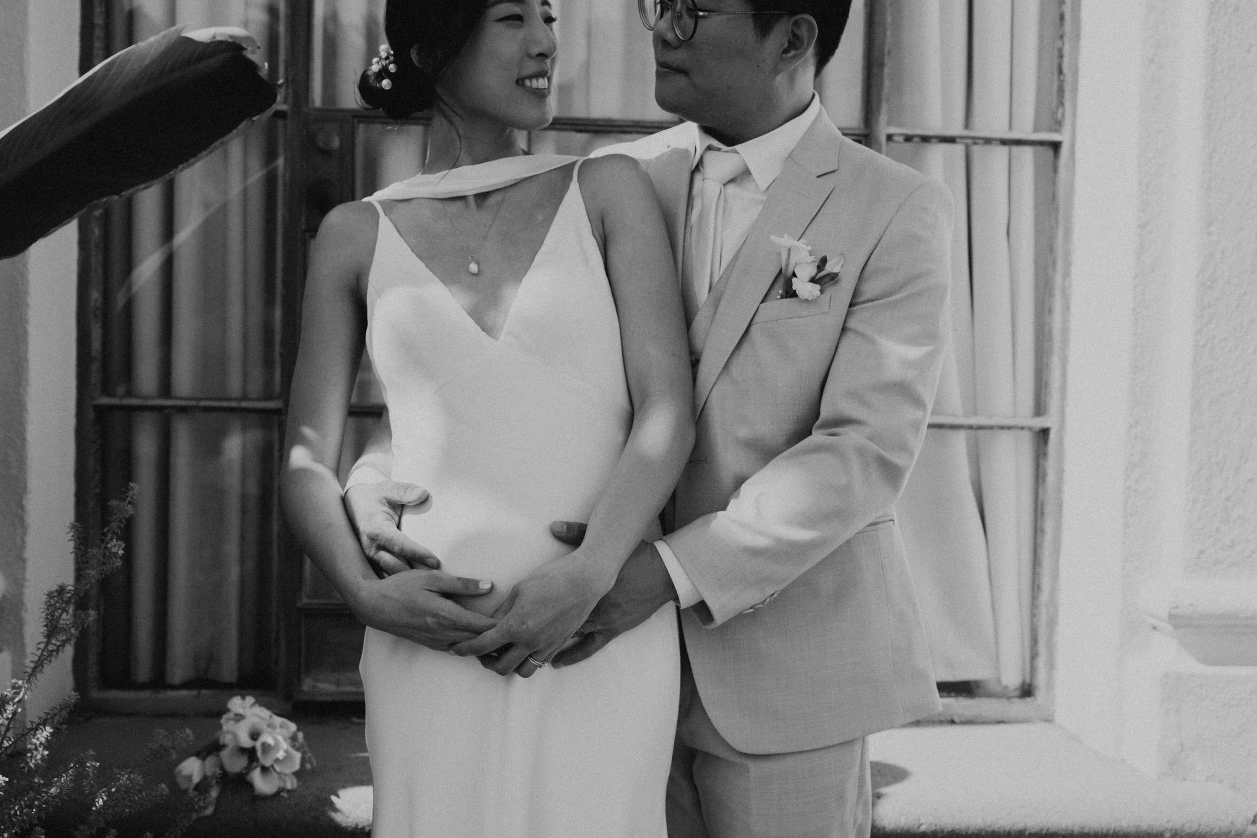 black and white photos of groom standing behind bride with his arms around her. The couple is looking at one another as they hold her belly bump