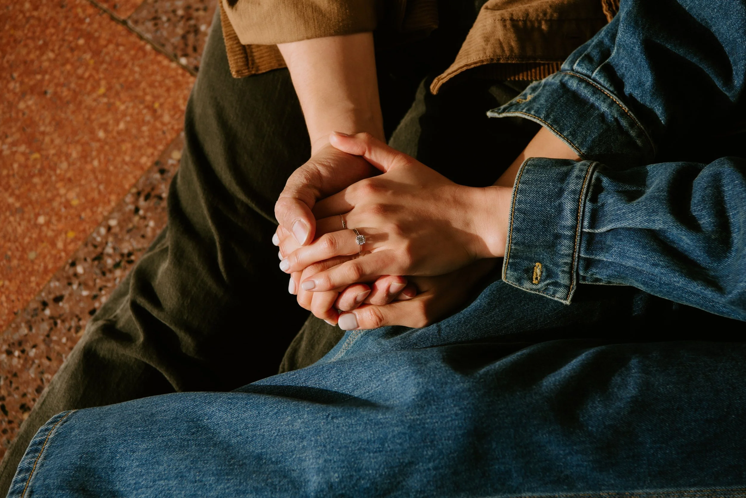 Close up of guy hold girls hands. An engagement ring can be seen