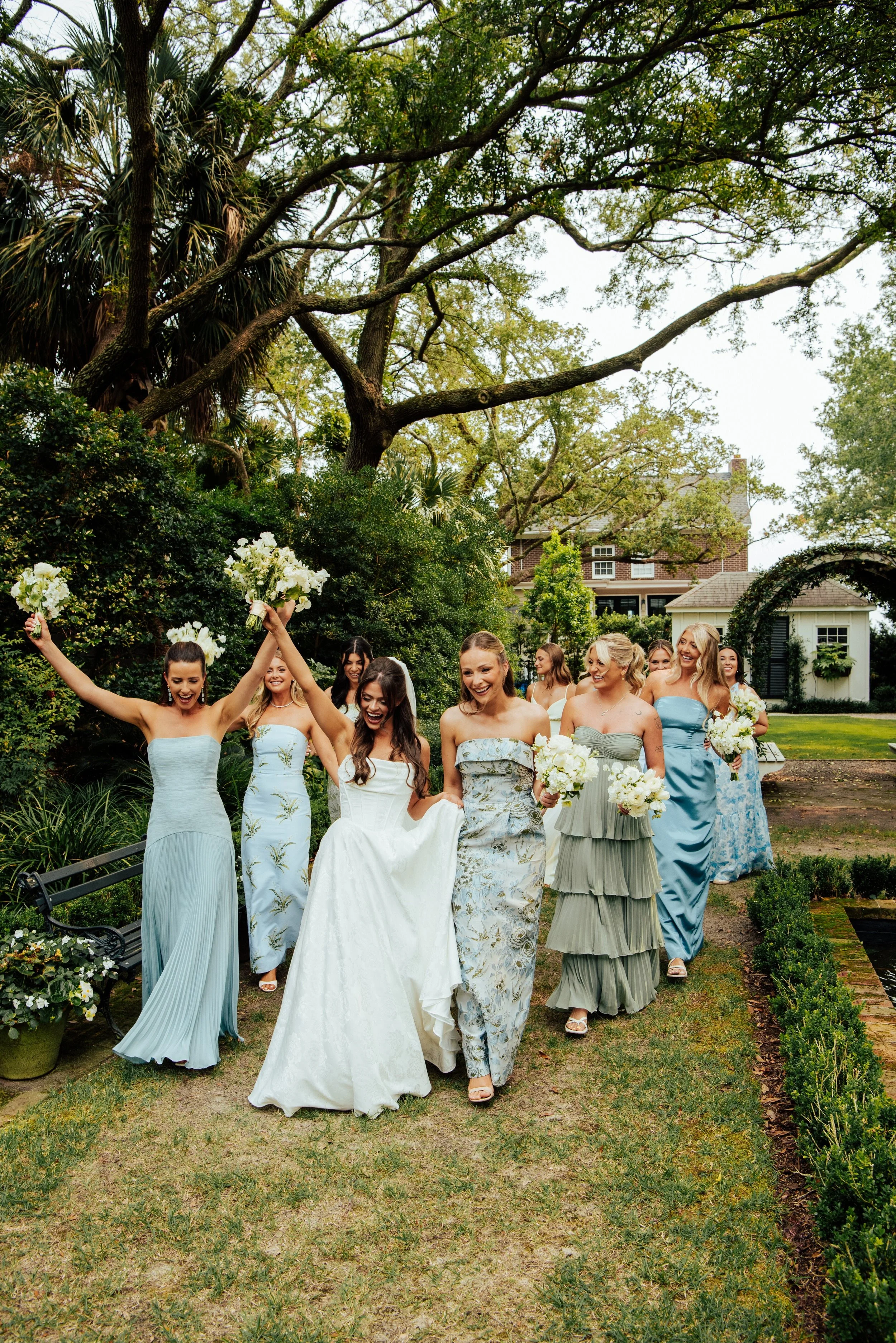 Bride walking with her bridesmaids who are in different shades of blue & green dresses